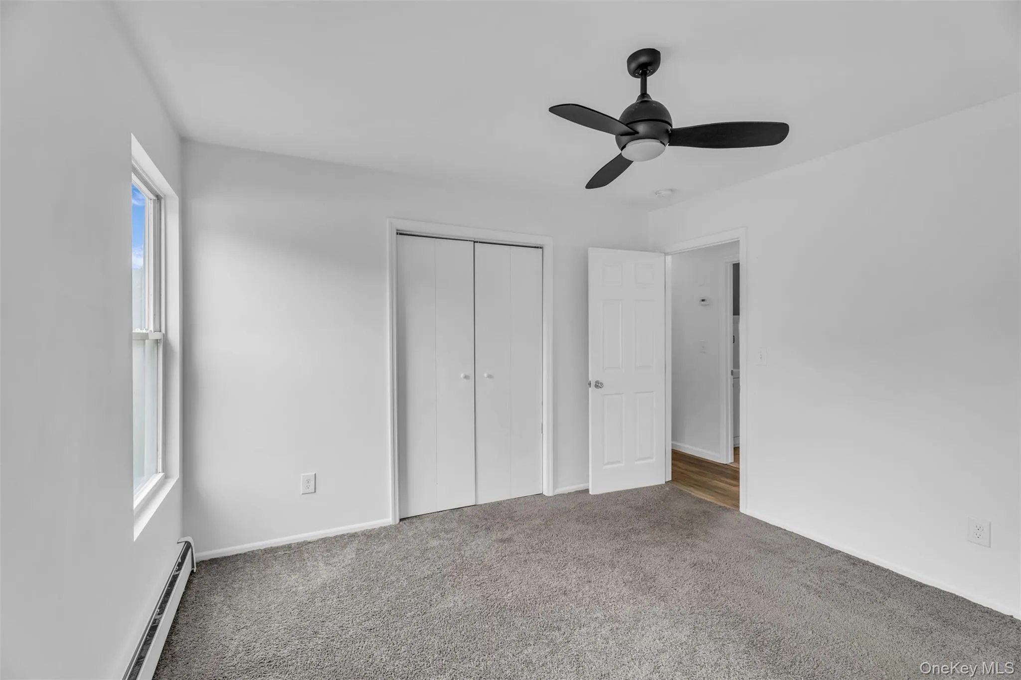 Unfurnished bedroom with baseboard heating, carpet, a ceiling fan, and a closet Unfurnished bedroom with baseboard heating, carpet, a ceiling fan, and a closet