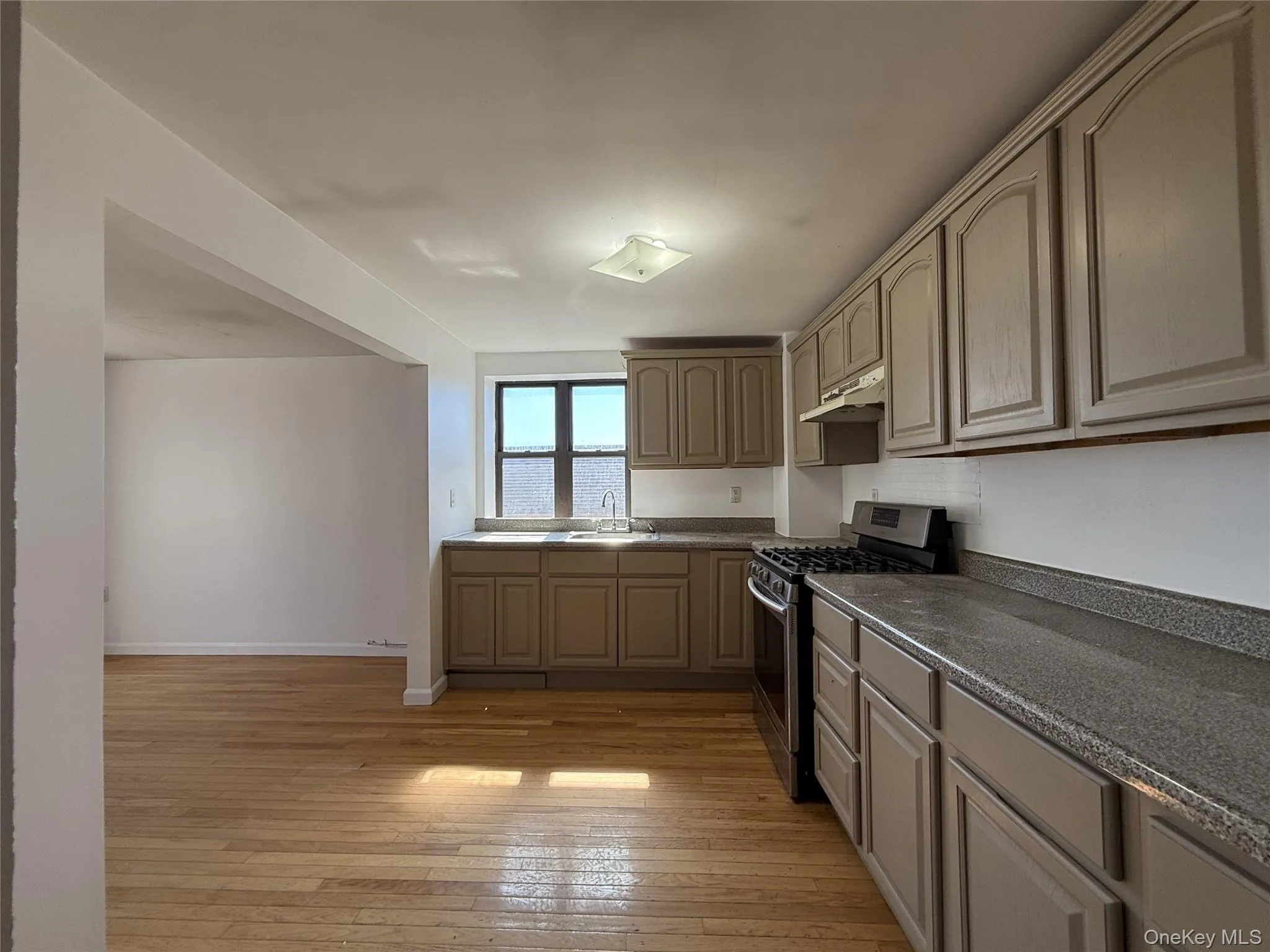 Kitchen with gas range, light wood-style floors, dark countertops, and under cabinet range hood Kitchen with gas range, light wood-style floors, dark countertops, and under cabinet range hood