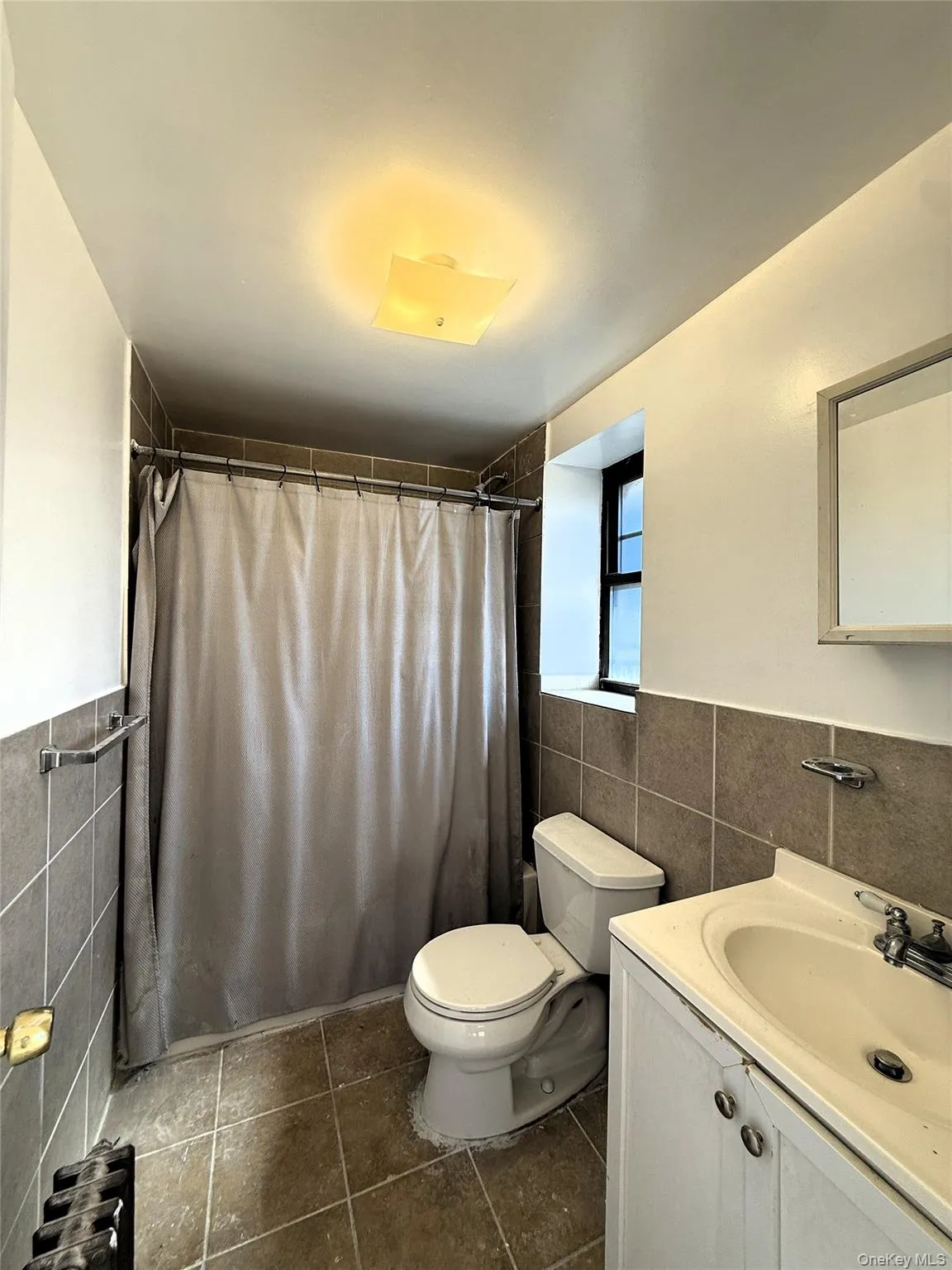 Bathroom with tile walls, vanity, wainscoting, radiator heating unit, and dark tile patterned floors Bathroom with tile walls, vanity, wainscoting, radiator heating unit, and dark tile patterned floors