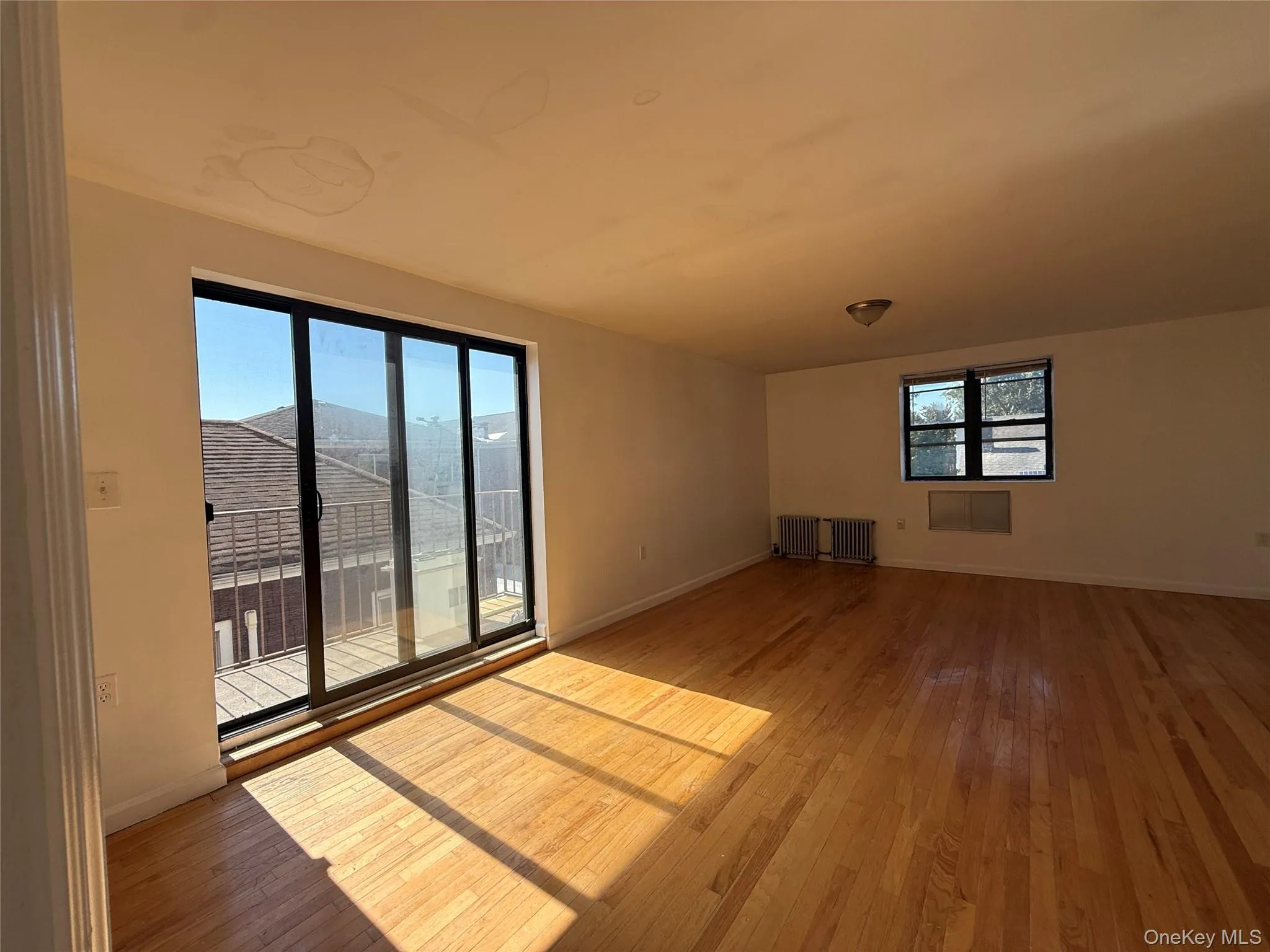 Unfurnished living room featuring light wood-type flooring and radiator Unfurnished living room featuring light wood-type flooring and radiator