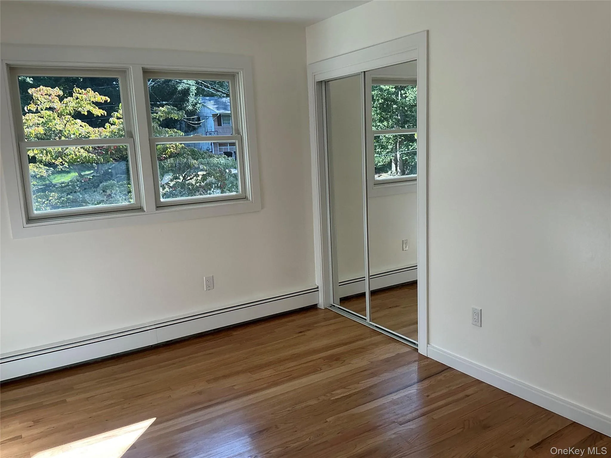 Unfurnished bedroom with baseboard heating, wood finished floors, and a closet Unfurnished bedroom with baseboard heating, wood finished floors, and a closet