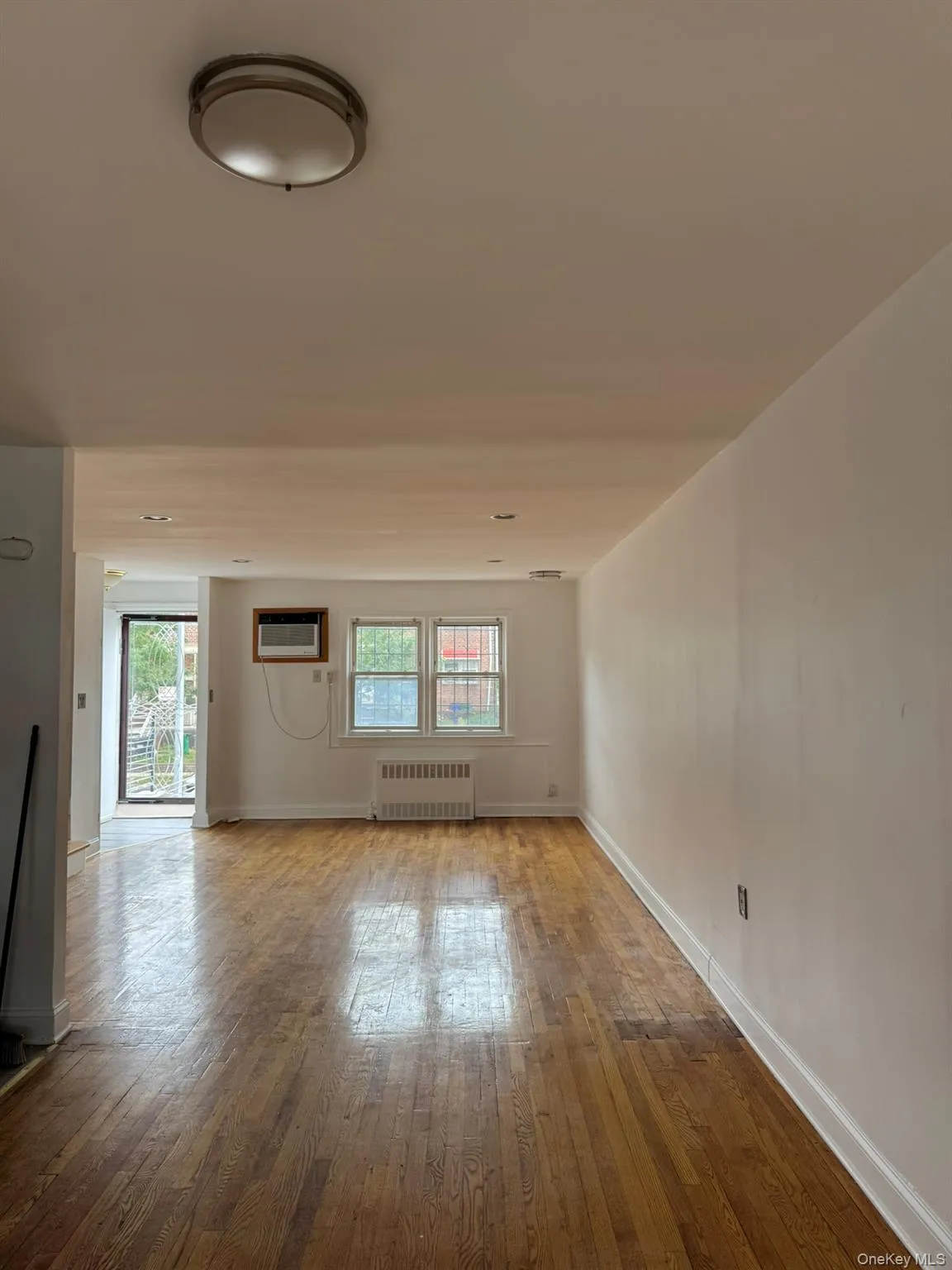 Unfurnished living room with healthy amount of natural light, wood-type flooring, radiator heating unit, and an AC wall unit Unfurnished living room with healthy amount of natural light, wood-type flooring, radiator heating unit, and an AC wall unit