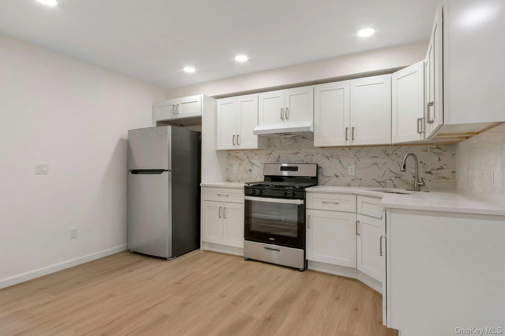 Kitchen with stainless steel appliances, white cabinets, decorative backsplash, light wood finished floors, and light stone countertops Kitchen with stainless steel appliances, white cabinets, decorative backsplash, light wood finished floors, and light stone countertops