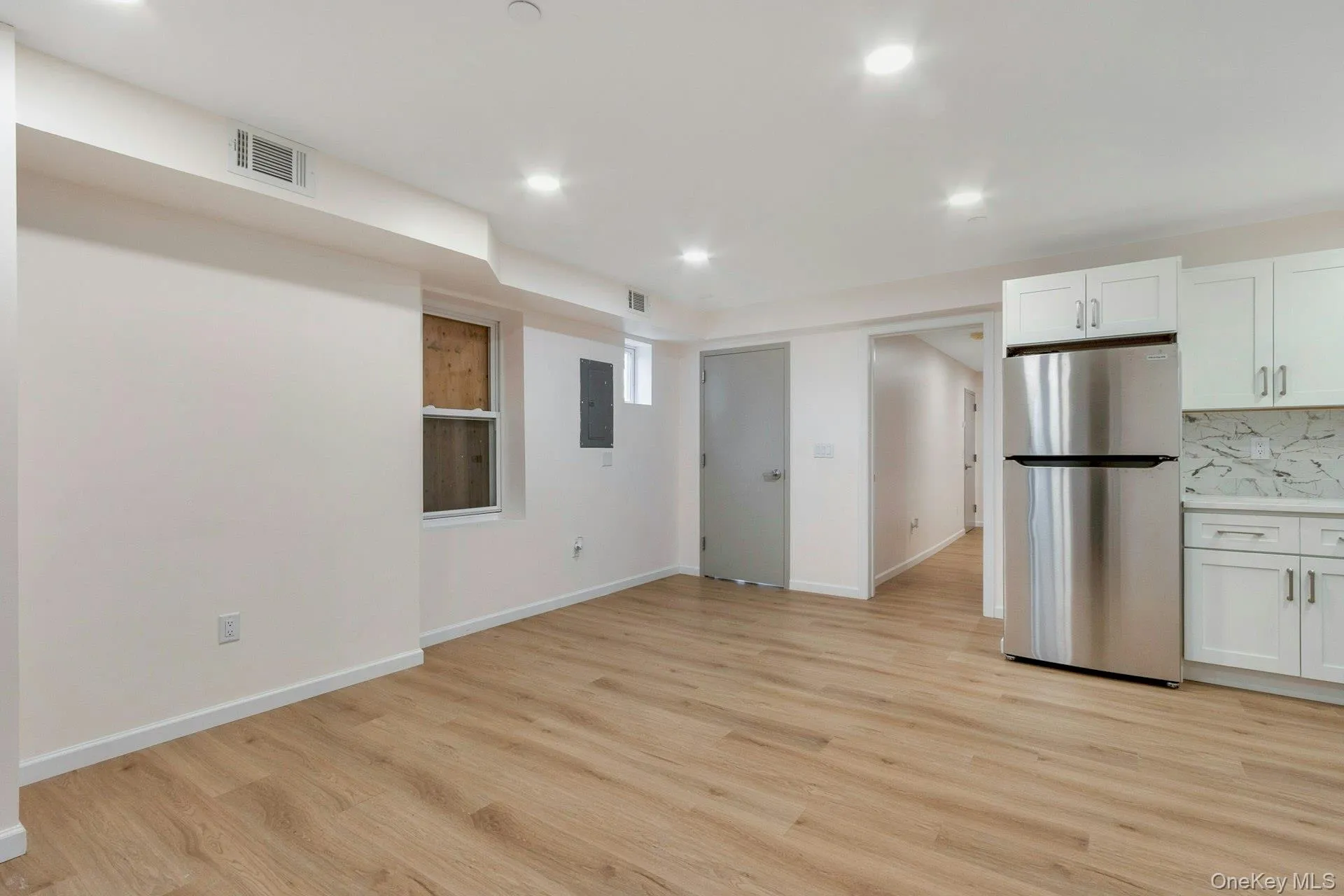 Kitchen with freestanding refrigerator, white cabinets, recessed lighting, light wood-style flooring, and tasteful backsplash Kitchen with freestanding refrigerator, white cabinets, recessed lighting, light wood-style flooring, and tasteful backsplash