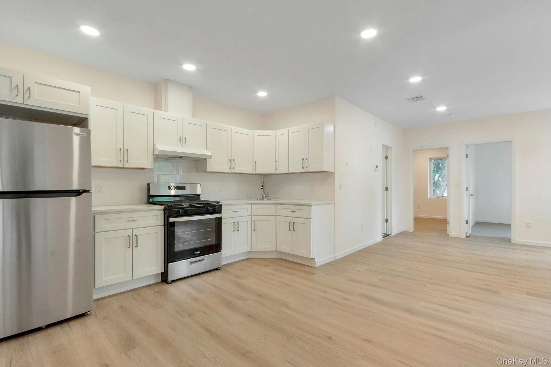 Kitchen with stainless steel appliances, decorative backsplash, light wood-style floors, white cabinetry, and recessed lighting Kitchen with stainless steel appliances, decorative backsplash, light wood-style floors, white cabinetry, and recessed lighting