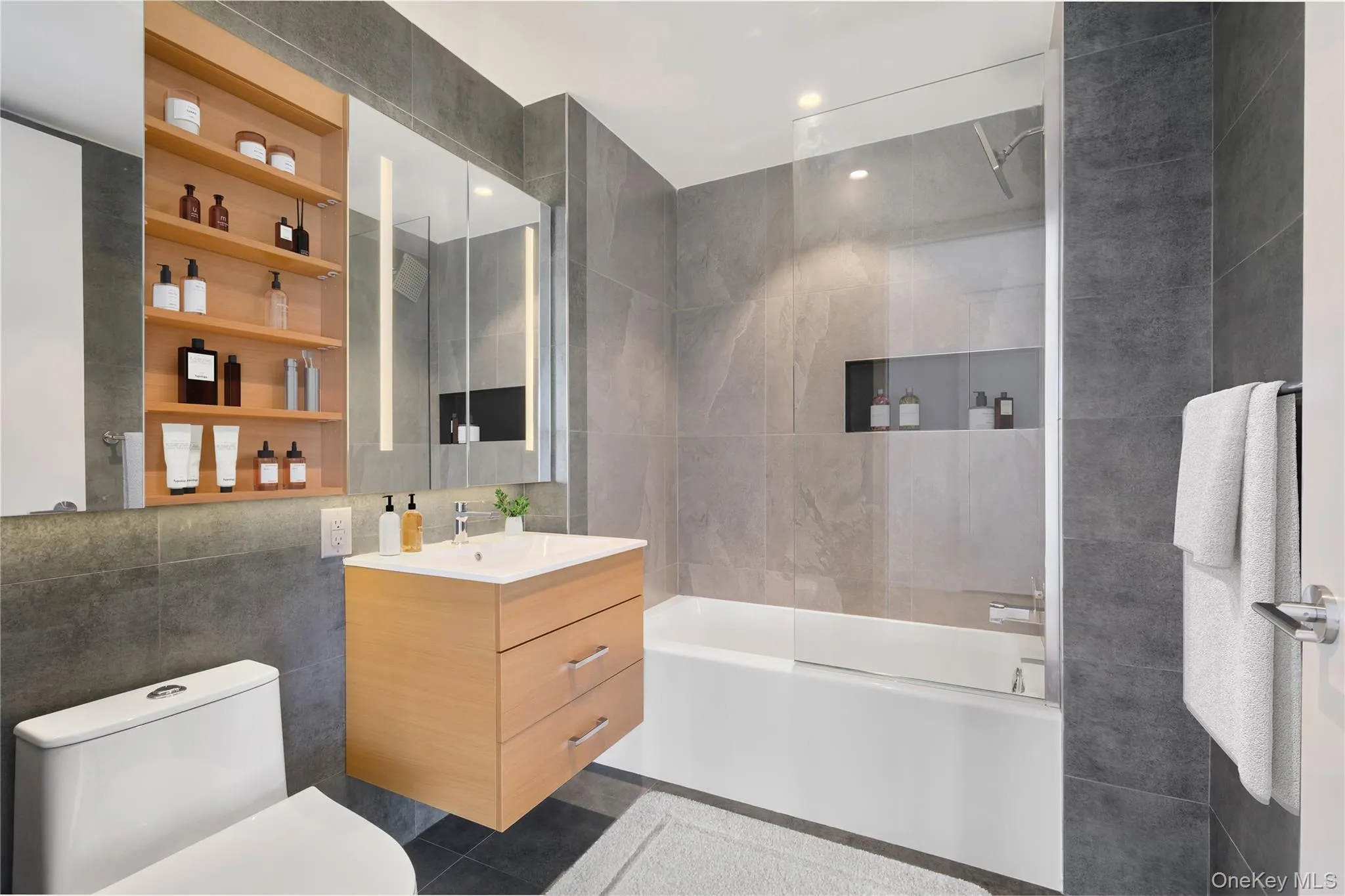 Full bathroom with tile walls, vanity, shower combination, and dark tile patterned flooring Full bathroom with tile walls, vanity, shower combination, and dark tile patterned flooring