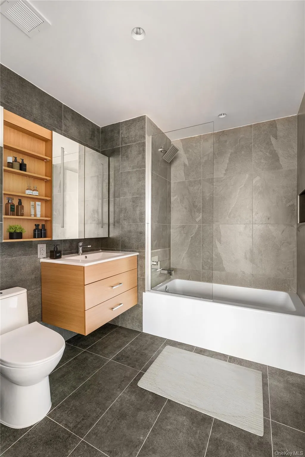 Bathroom with tile walls, shower combination, vanity, dark tile patterned floors, and recessed lighting Bathroom with tile walls, shower combination, vanity, dark tile patterned floors, and recessed lighting