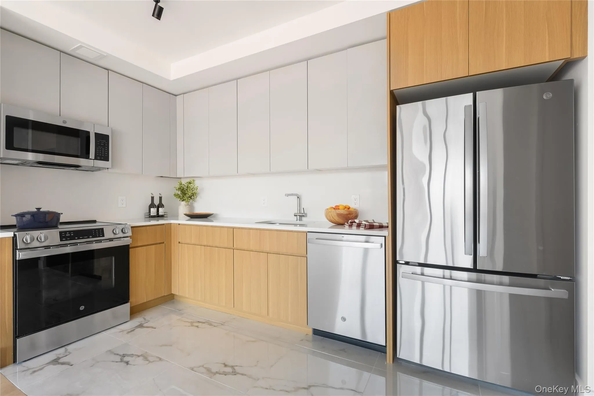 Kitchen featuring modern cabinets, appliances with stainless steel finishes, light marble finish floors, and white cabinets Kitchen featuring modern cabinets, appliances with stainless steel finishes, light marble finish floors, and white cabinets