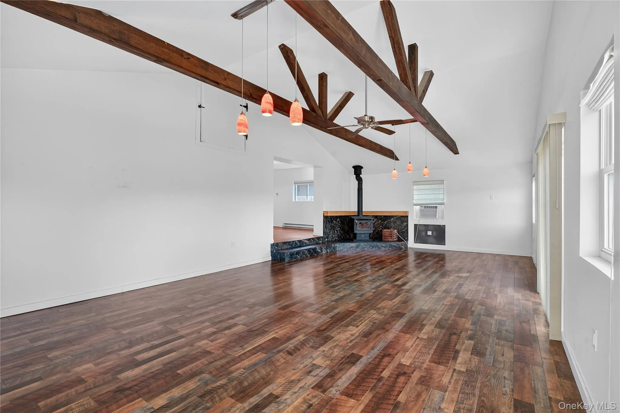 Unfurnished living room with a wood stove, beamed ceiling, high vaulted ceiling, ceiling fan, and dark wood-style floors Unfurnished living room with a wood stove, beamed ceiling, high vaulted ceiling, ceiling fan, and dark wood-style floors
