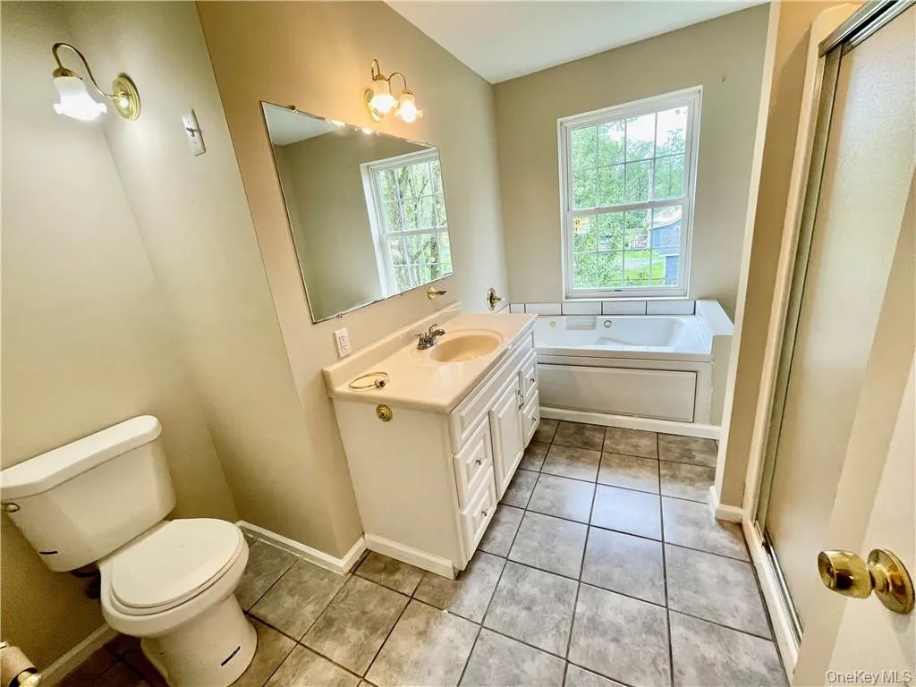 Bathroom featuring toilet, tile patterned floors, vanity, and a bathing tub Bathroom featuring toilet, tile patterned floors, vanity, and a bathing tub