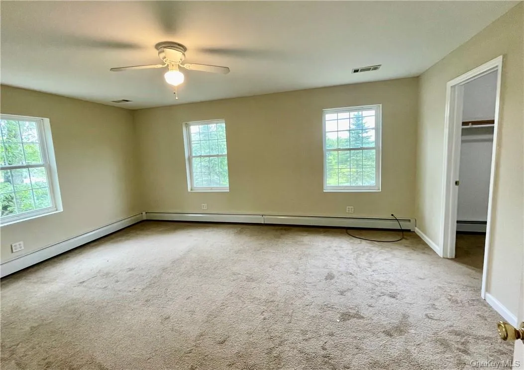 Unfurnished bedroom featuring a baseboard heating unit, ceiling fan, a walk in closet, and light carpet Unfurnished bedroom featuring a baseboard heating unit, ceiling fan, a walk in closet, and light carpet