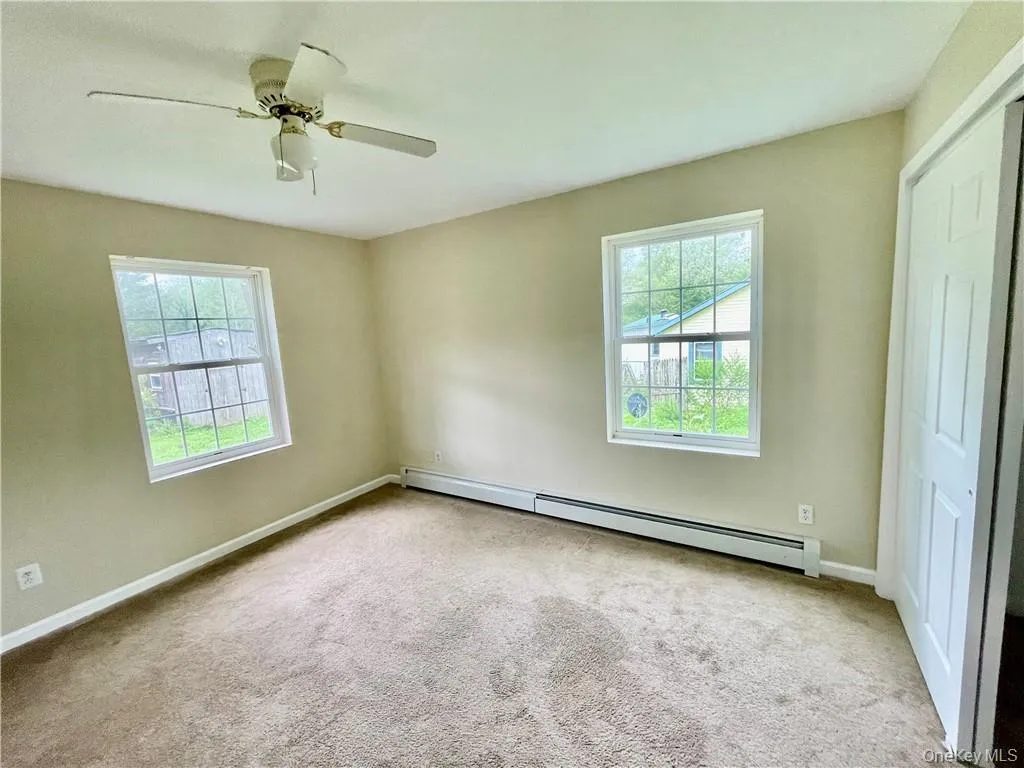 Unfurnished bedroom featuring ceiling fan, baseboard heating, light carpet, and a closet Unfurnished bedroom featuring ceiling fan, baseboard heating, light carpet, and a closet