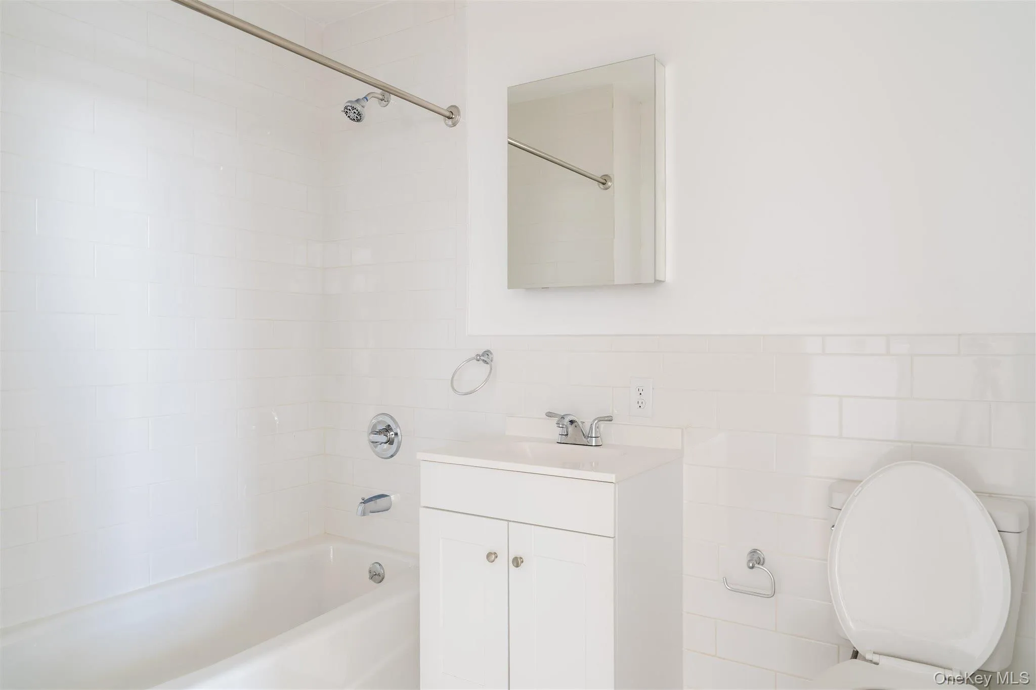 Full bath featuring bathing tub / shower combination, vanity, tile walls, and a wainscoted wall Full bath featuring bathing tub / shower combination, vanity, tile walls, and a wainscoted wall