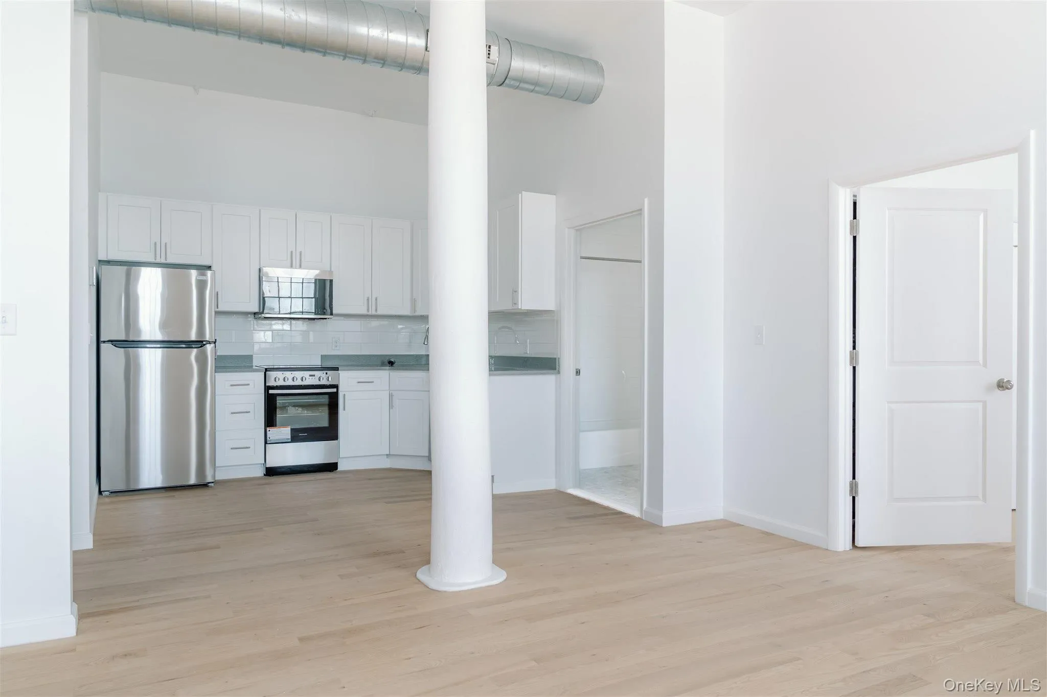 Kitchen with a towering ceiling, appliances with stainless steel finishes, backsplash, light wood-style floors, and white cabinetry Kitchen with a towering ceiling, appliances with stainless steel finishes, backsplash, light wood-style floors, and white cabinetry