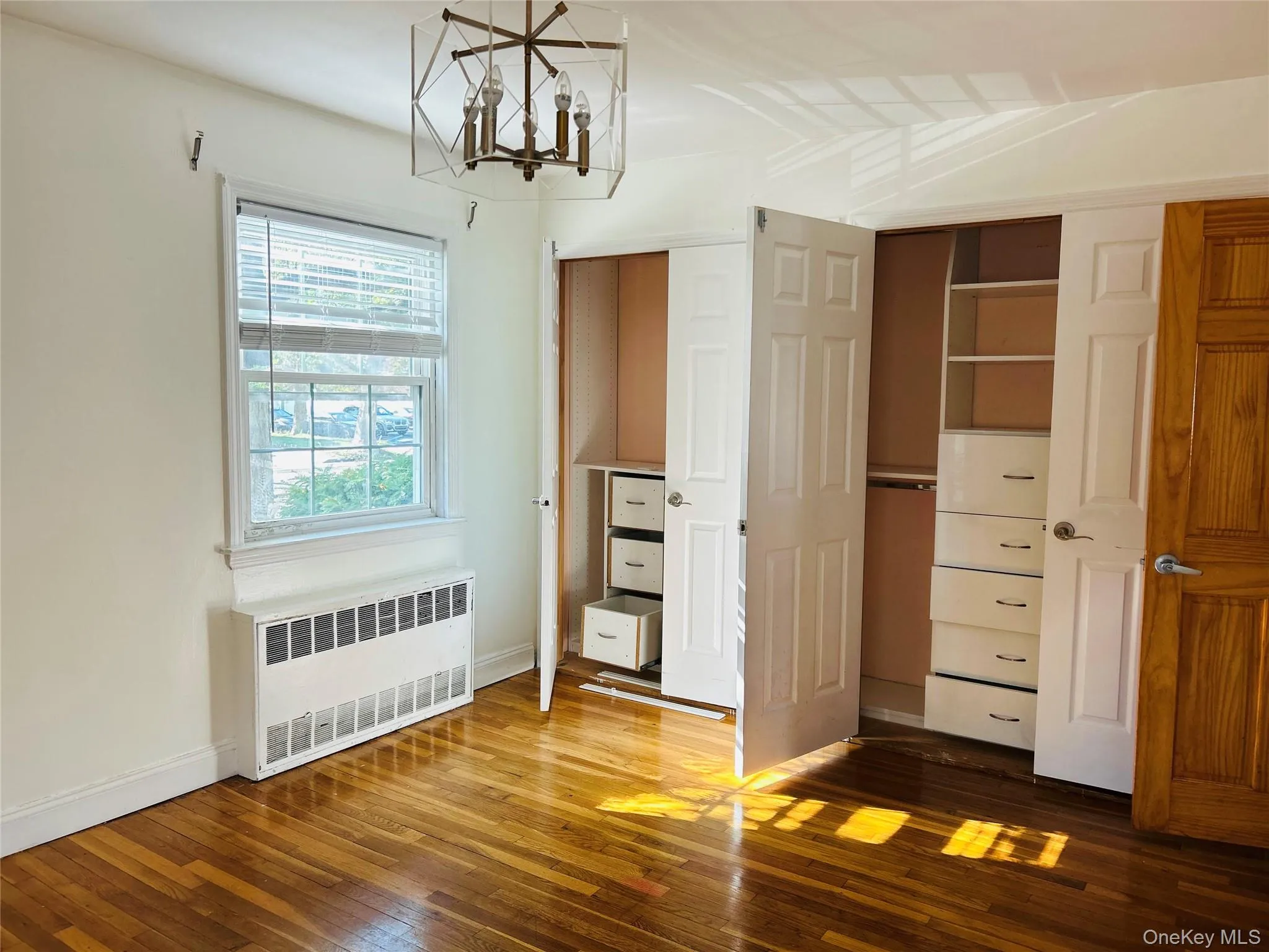 Unfurnished bedroom featuring radiator heating unit, hardwood / wood-style flooring, a chandelier, and a closet Unfurnished bedroom featuring radiator heating unit, hardwood / wood-style flooring, a chandelier, and a closet