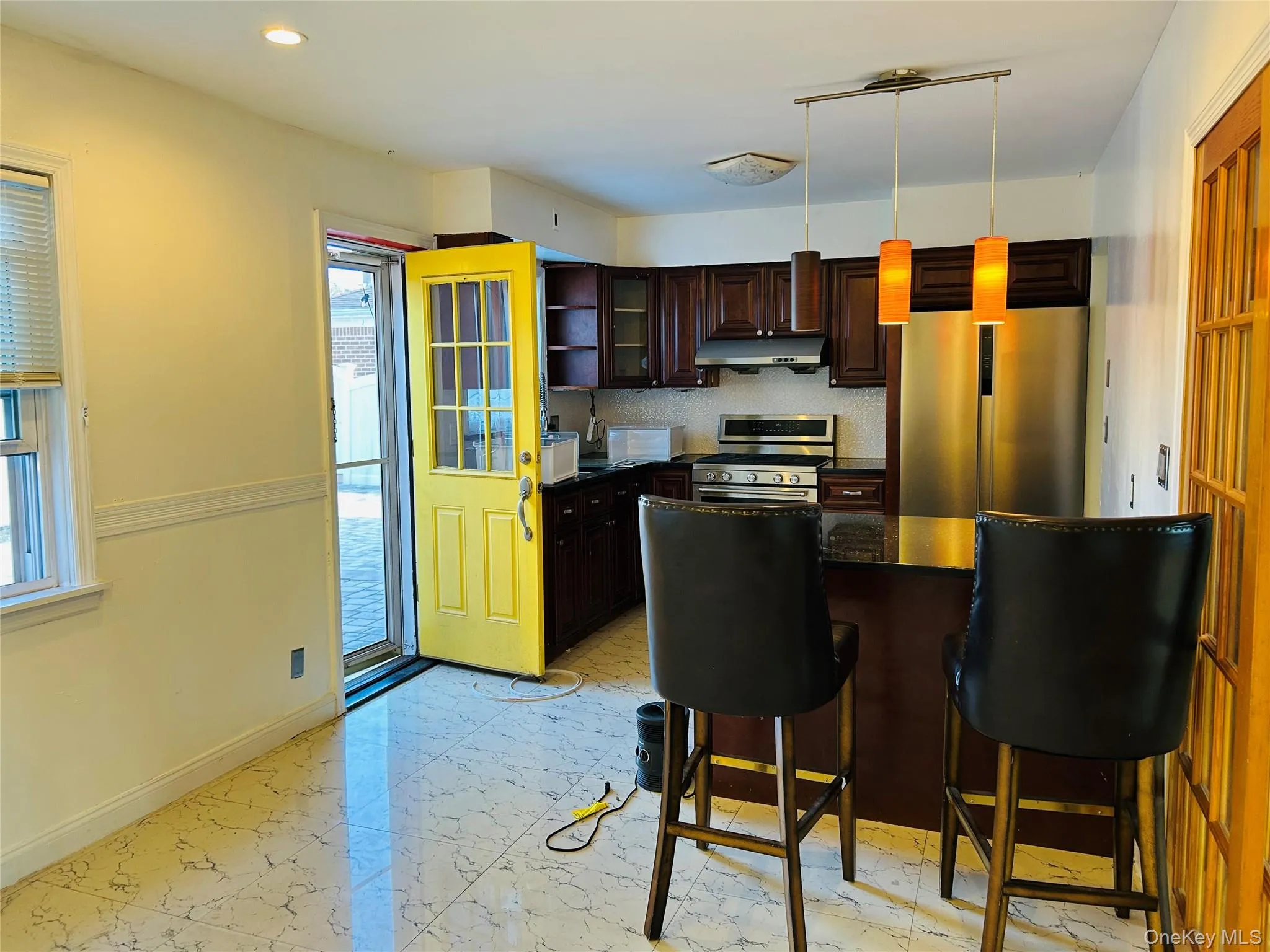 Kitchen featuring dark brown cabinets, appliances with stainless steel finishes, a breakfast bar, hanging light fixtures, and glass insert cabinets Kitchen featuring dark brown cabinets, appliances with stainless steel finishes, a breakfast bar, hanging light fixtures, and glass insert cabinets