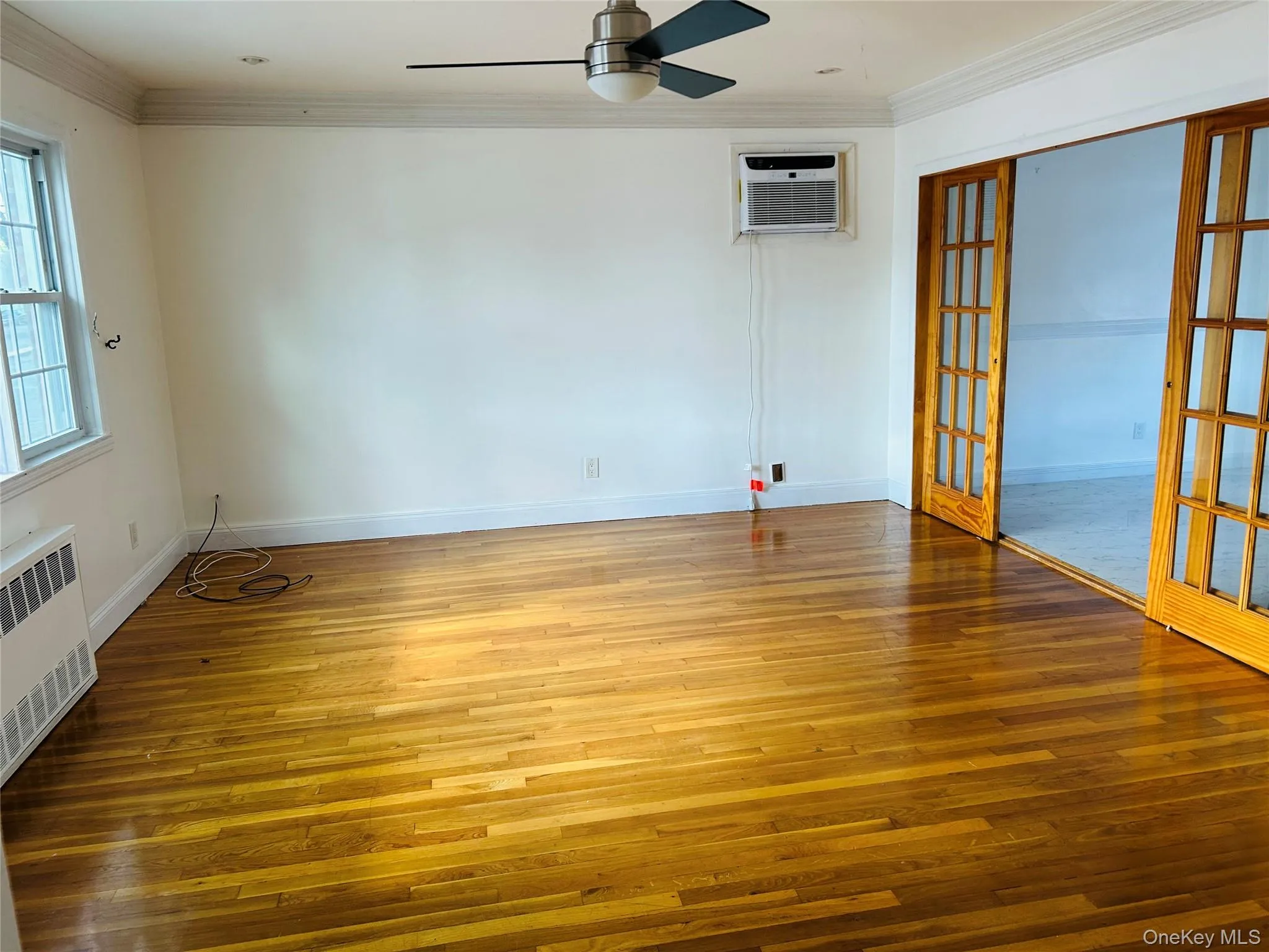 Spare room featuring ornamental molding, hardwood / wood-style floors, radiator heating unit, ceiling fan, and french doors Spare room featuring ornamental molding, hardwood / wood-style floors, radiator heating unit, ceiling fan, and french doors