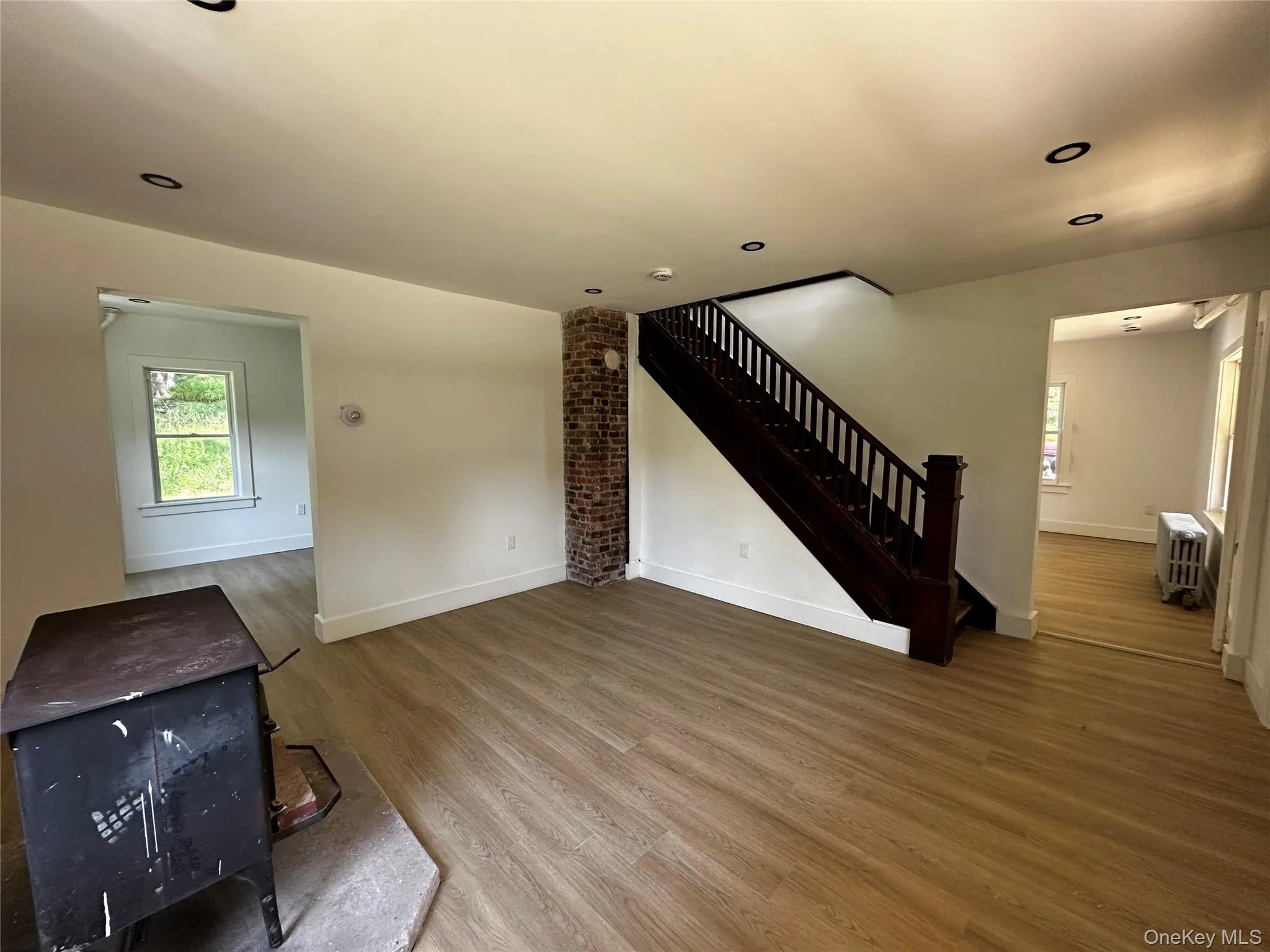 Unfurnished living room with a wood stove, wood finished floors, stairs, recessed lighting, and radiator Unfurnished living room with a wood stove, wood finished floors, stairs, recessed lighting, and radiator