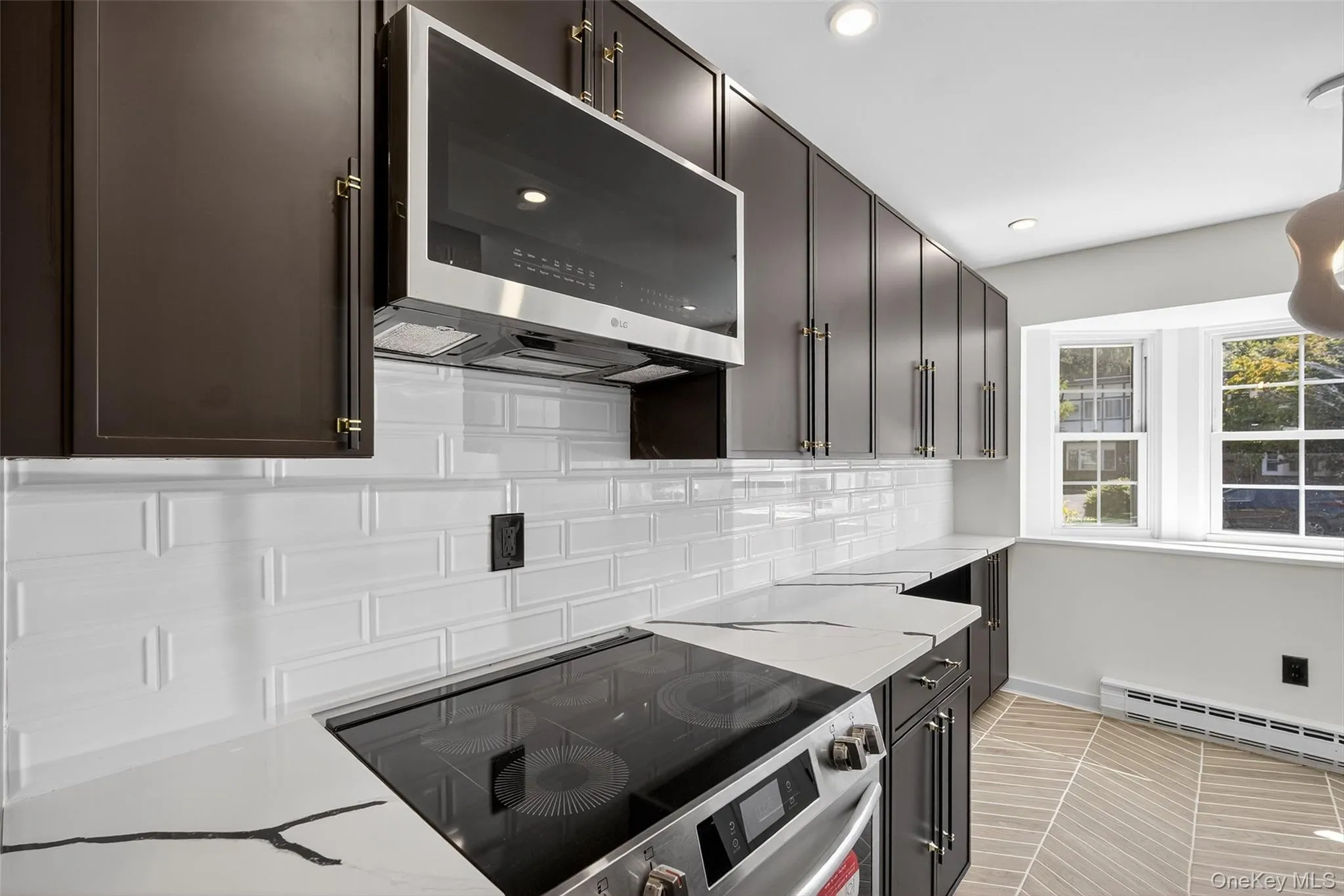Kitchen with stainless steel appliances, tasteful backsplash, a baseboard radiator, light tile patterned floors, and light stone countertops Kitchen with stainless steel appliances, tasteful backsplash, a baseboard radiator, light tile patterned floors, and light stone countertops