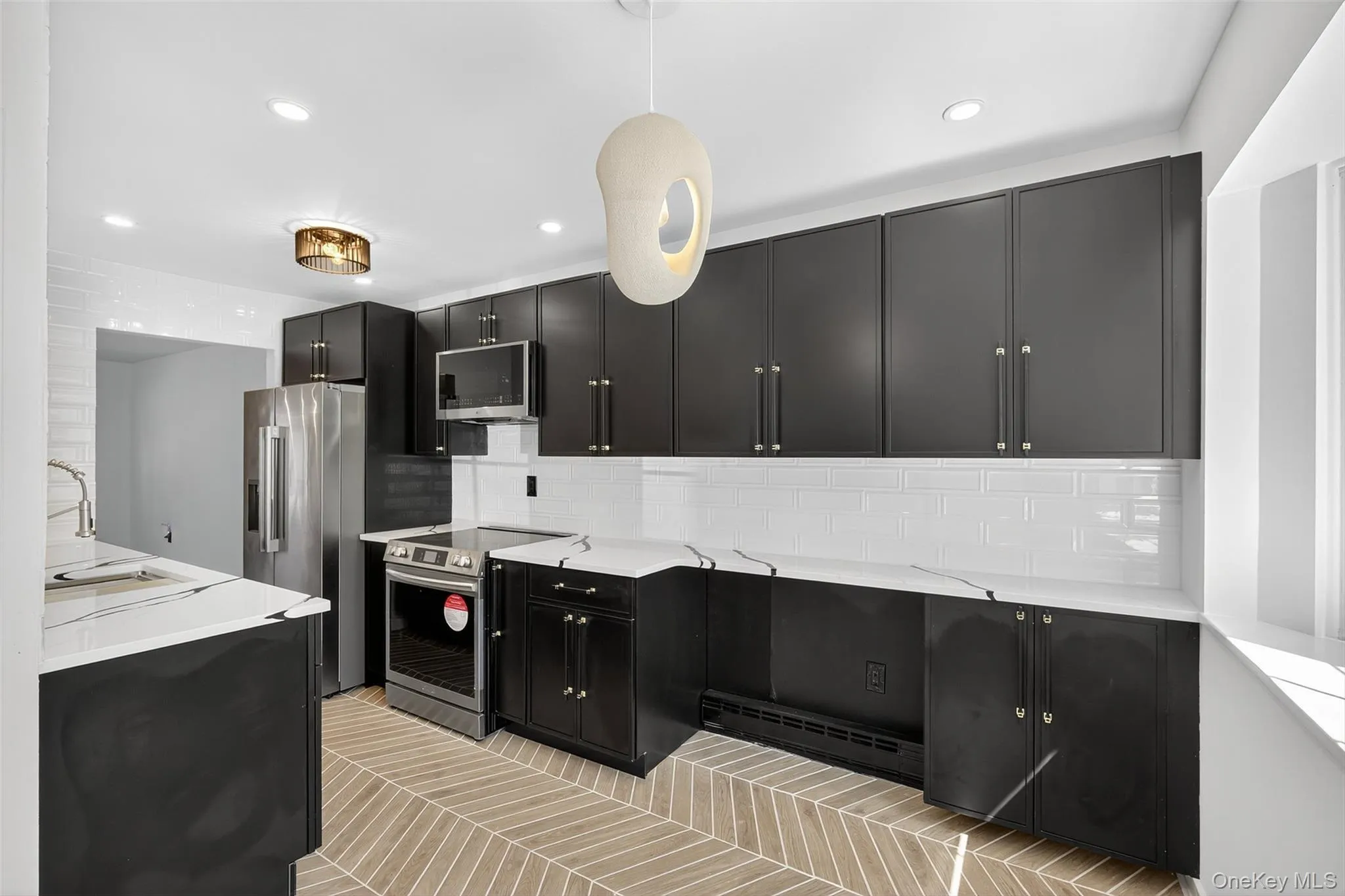Kitchen with dark cabinetry, backsplash, stainless steel appliances, light stone counters, and recessed lighting Kitchen with dark cabinetry, backsplash, stainless steel appliances, light stone counters, and recessed lighting