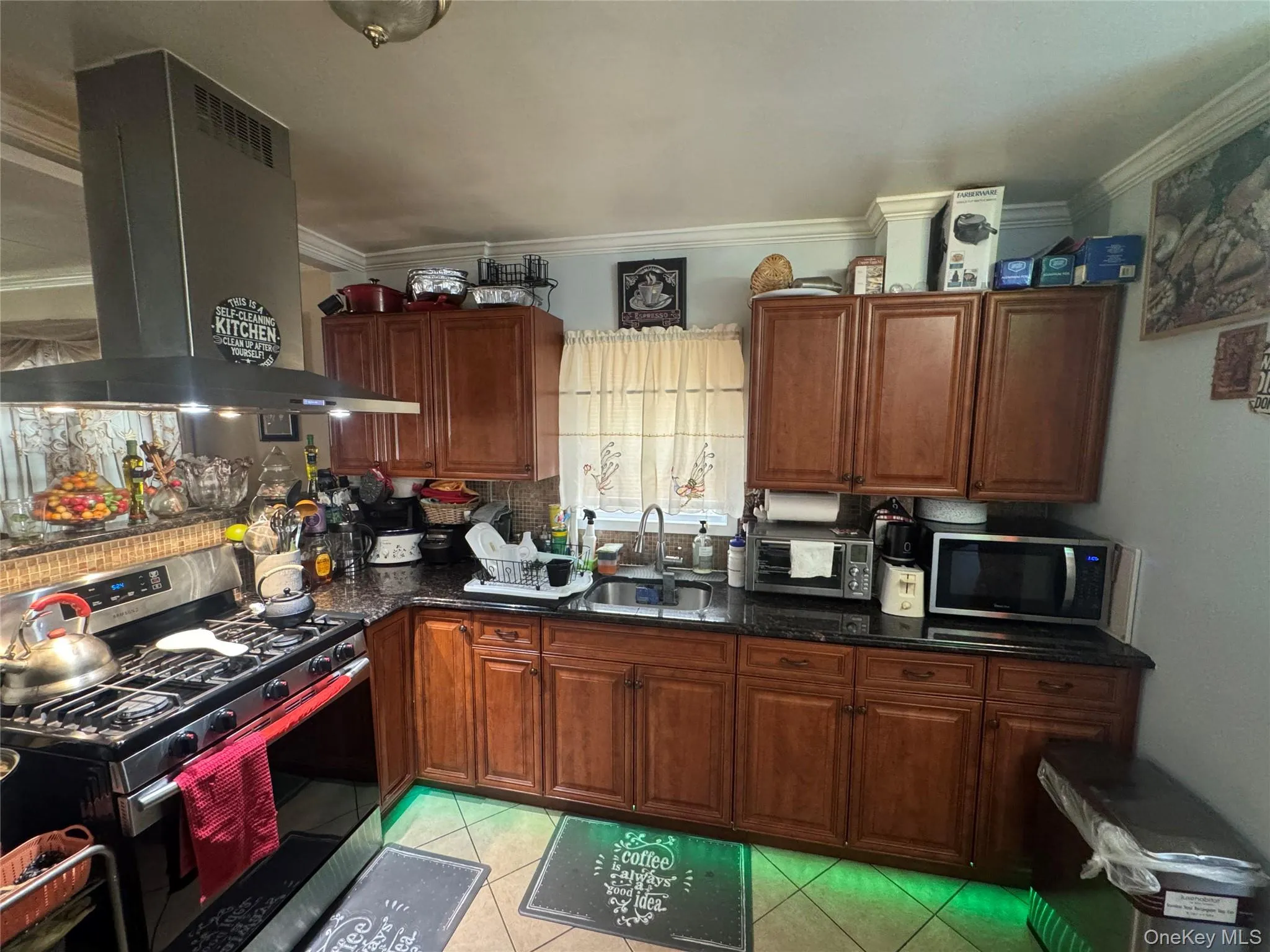 Kitchen with appliances with stainless steel finishes, island exhaust hood, light tile patterned flooring, crown molding, and dark stone counters Kitchen with appliances with stainless steel finishes, island exhaust hood, light tile patterned flooring, crown molding, and dark stone counters