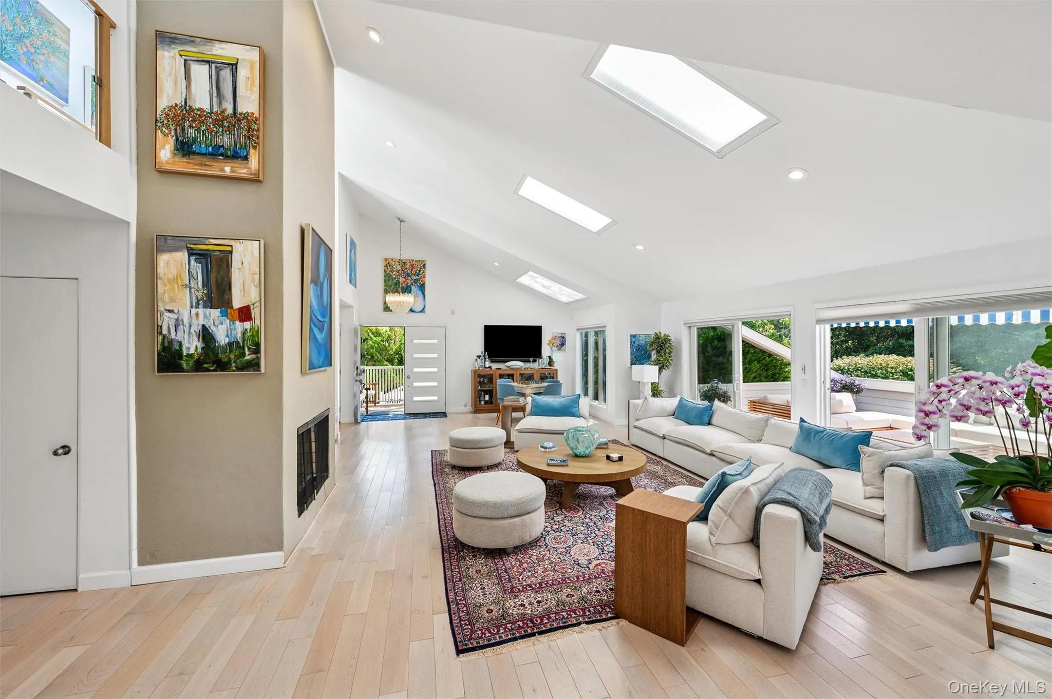Living area with a skylight, a fireplace, light wood-style flooring, high vaulted ceiling, and recessed lighting Living area with a skylight, a fireplace, light wood-style flooring, high vaulted ceiling, and recessed lighting