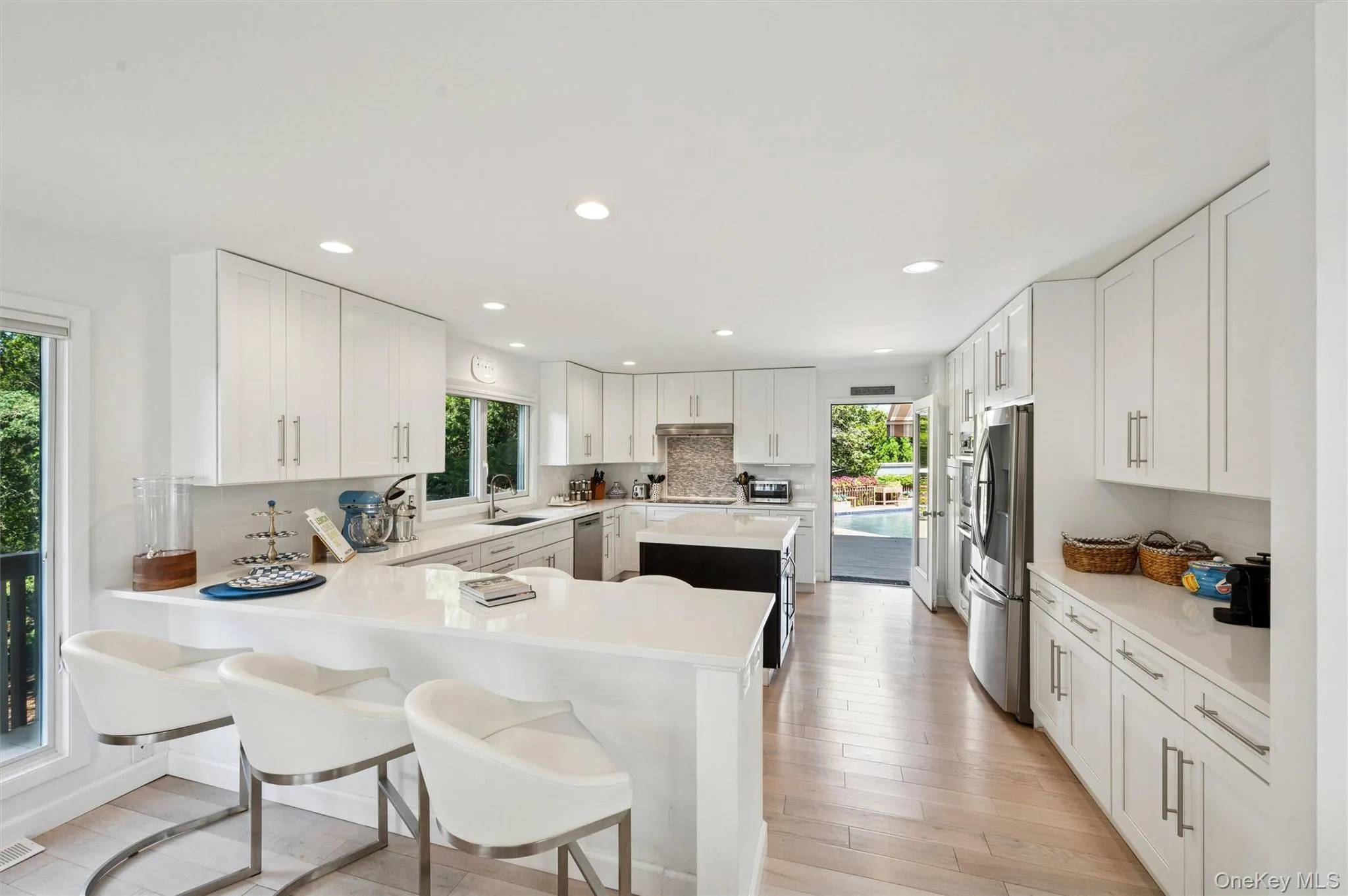 Kitchen with backsplash, a breakfast bar, white cabinetry, light wood-style floors, and recessed lighting Kitchen with backsplash, a breakfast bar, white cabinetry, light wood-style floors, and recessed lighting