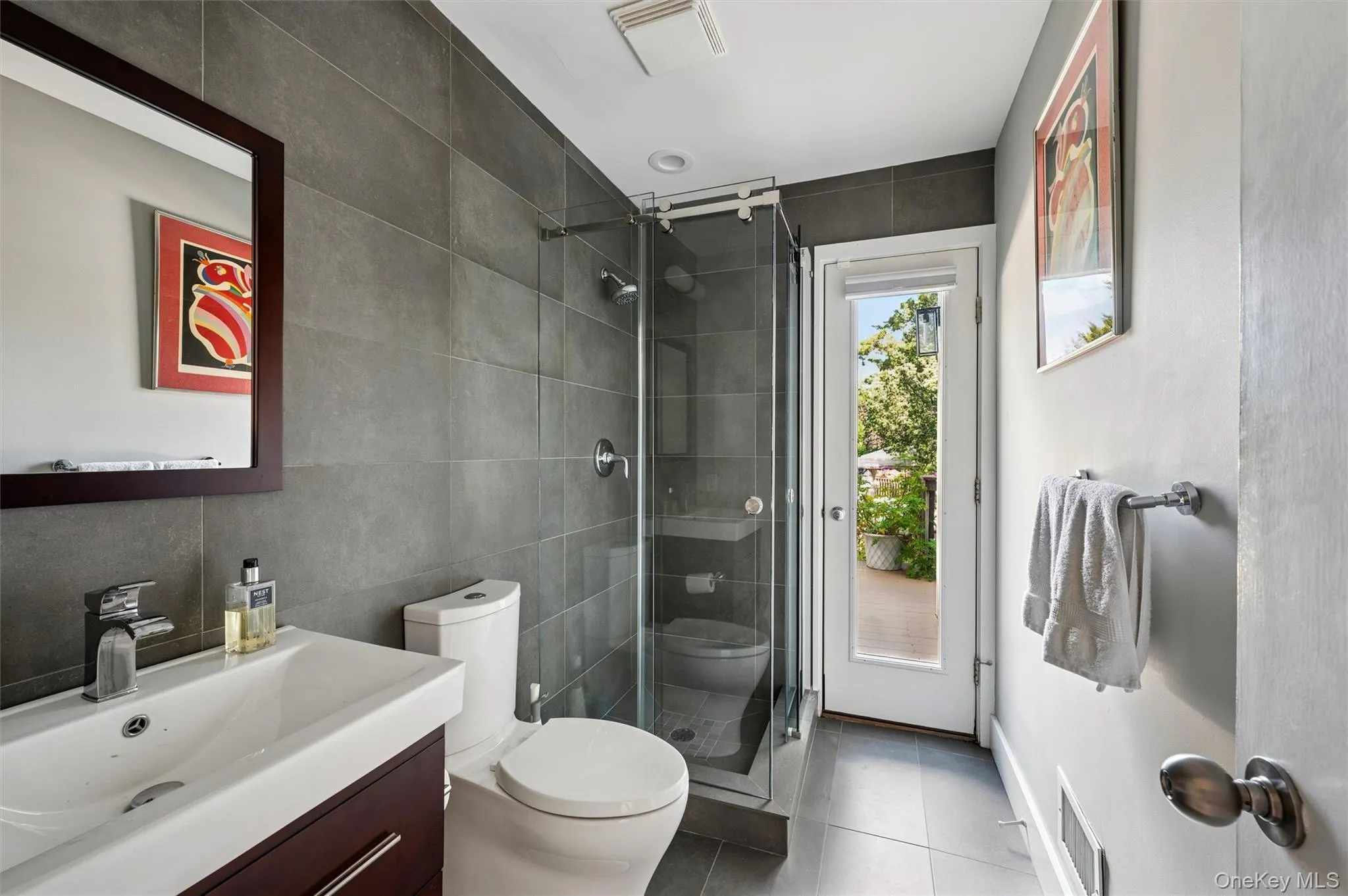 Full bath featuring tile walls, a shower stall, vanity, and dark tile patterned floors Full bath featuring tile walls, a shower stall, vanity, and dark tile patterned floors