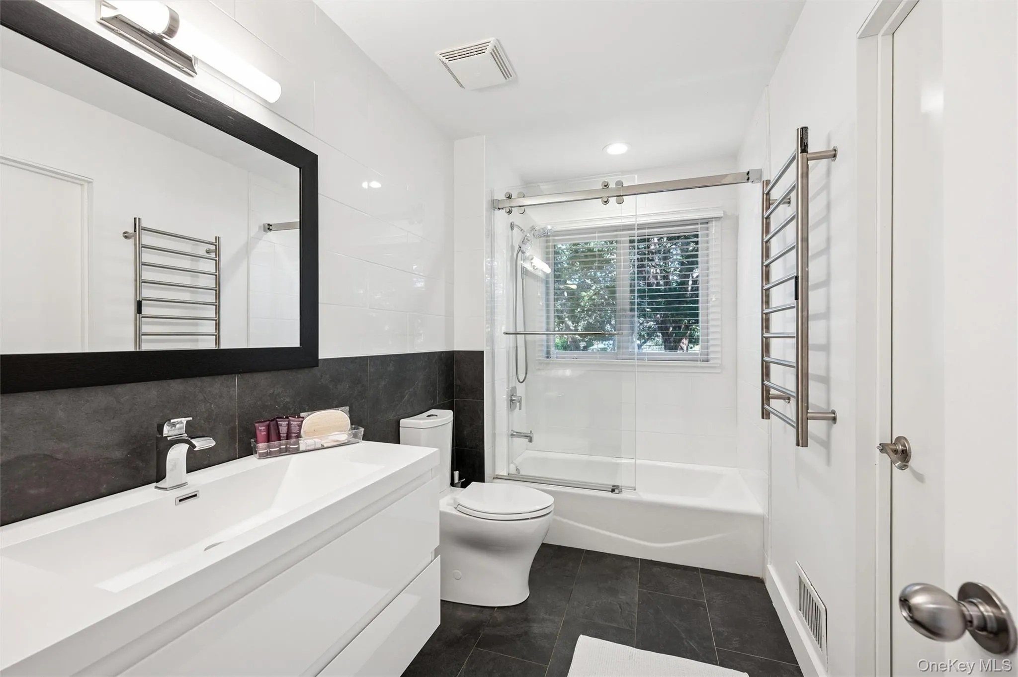Full bathroom with shower / bath combination with glass door, vanity, a towel warming rack, radiator heating unit, and tile walls Full bathroom with shower / bath combination with glass door, vanity, a towel warming rack, radiator heating unit, and tile walls