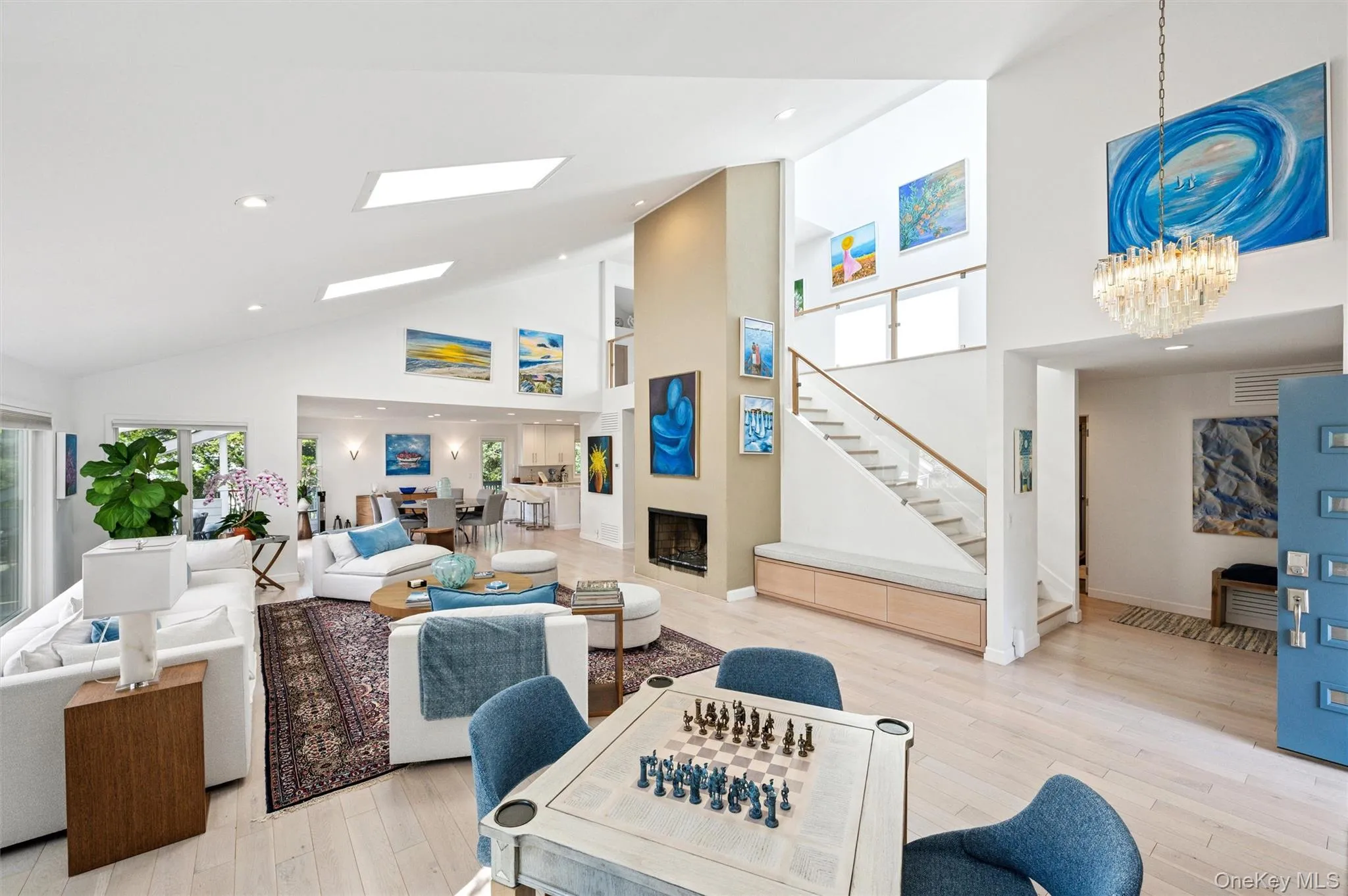 Living area featuring high vaulted ceiling, light wood-style flooring, stairway, recessed lighting, and a fireplace Living area featuring high vaulted ceiling, light wood-style flooring, stairway, recessed lighting, and a fireplace