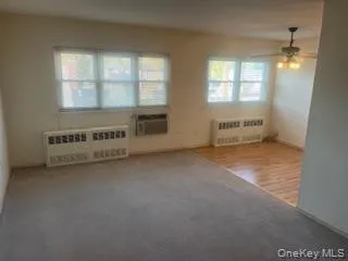 Unfurnished living room with new carpeting into dining area with ceiling fan, and a wall-mounted air conditioner. Unfurnished living room with new carpeting into dining area with ceiling fan, and a wall-mounted air conditioner.