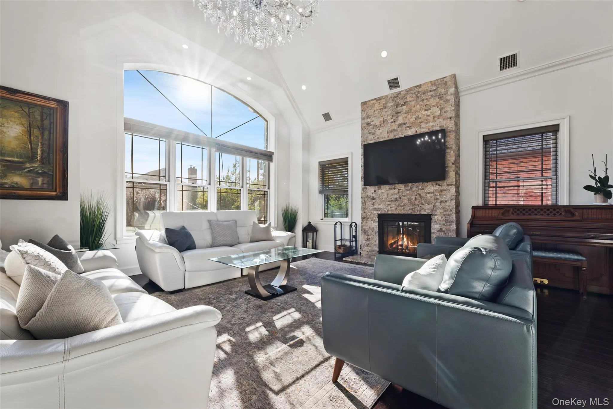 Living room with high vaulted ceiling, a stone fireplace, a chandelier, crown molding, and recessed lighting Living room with high vaulted ceiling, a stone fireplace, a chandelier, crown molding, and recessed lighting
