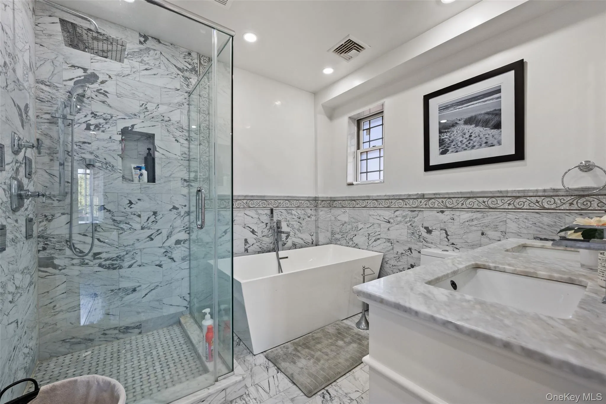 Full bath with tile walls, a freestanding tub, double vanity, a marble finish shower, and wainscoting Full bath with tile walls, a freestanding tub, double vanity, a marble finish shower, and wainscoting