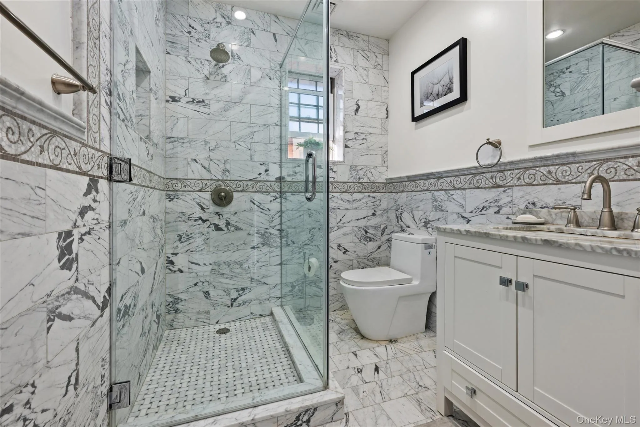 Bathroom featuring tile walls, a marble finish shower, vanity, and light marble finish floors Bathroom featuring tile walls, a marble finish shower, vanity, and light marble finish floors