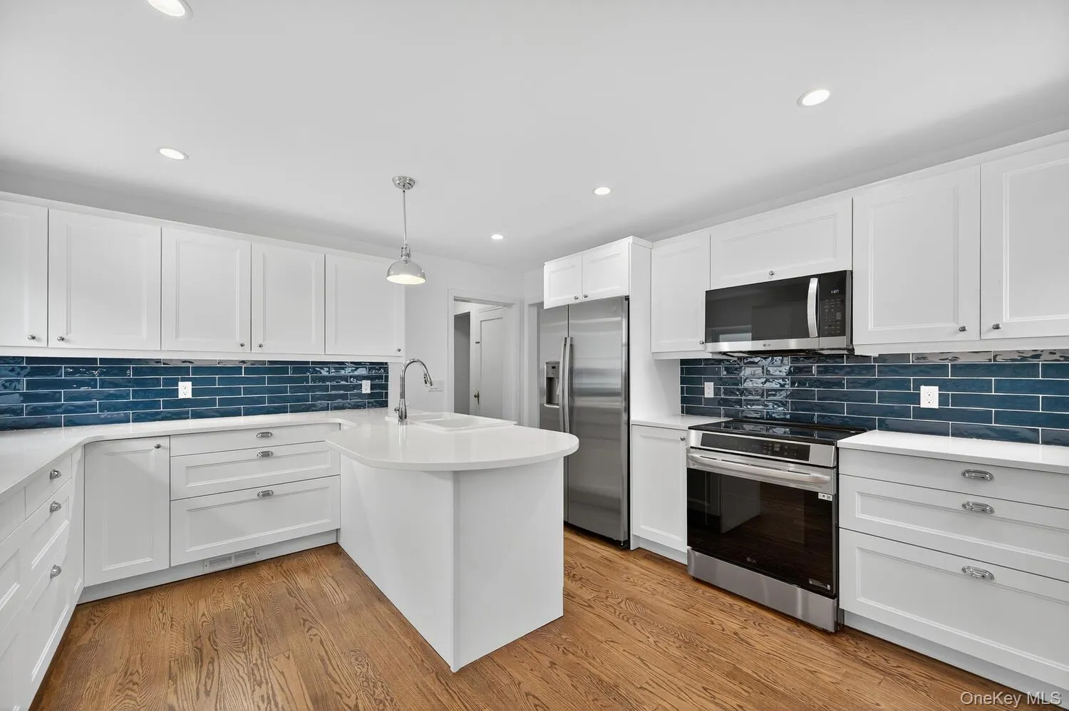 Kitchen featuring white cabinets, stainless steel appliances, a peninsula, pendant lighting, and decorative backsplash Kitchen featuring white cabinets, stainless steel appliances, a peninsula, pendant lighting, and decorative backsplash