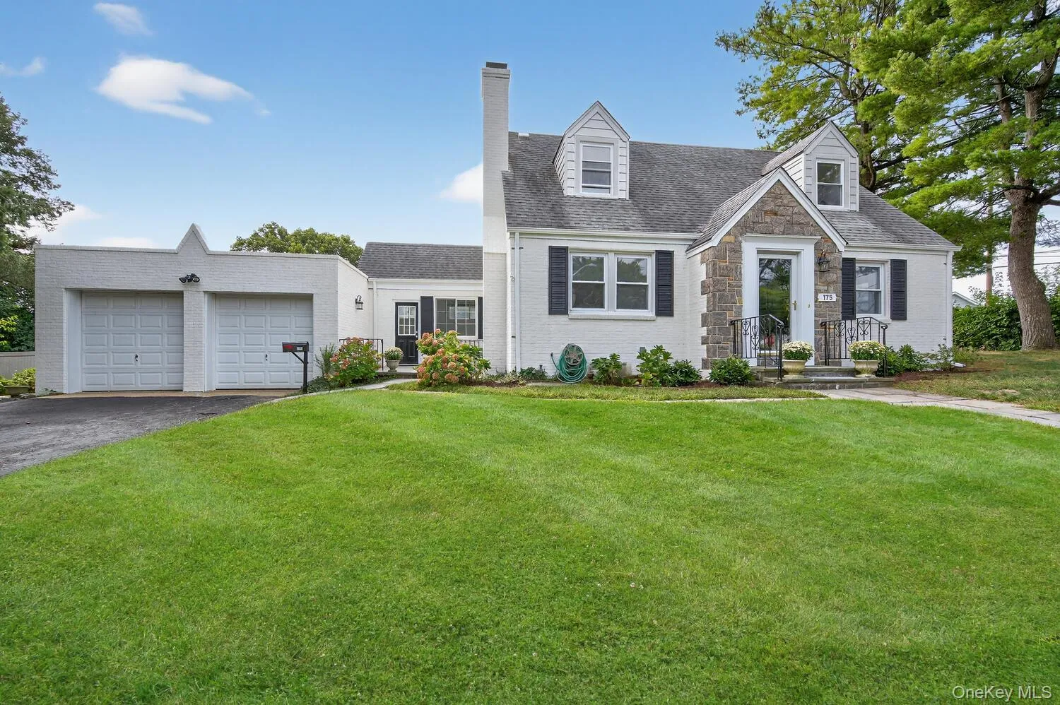 New england style home with a front yard, a chimney, stone siding, and a garage New england style home with a front yard, a chimney, stone siding, and a garage