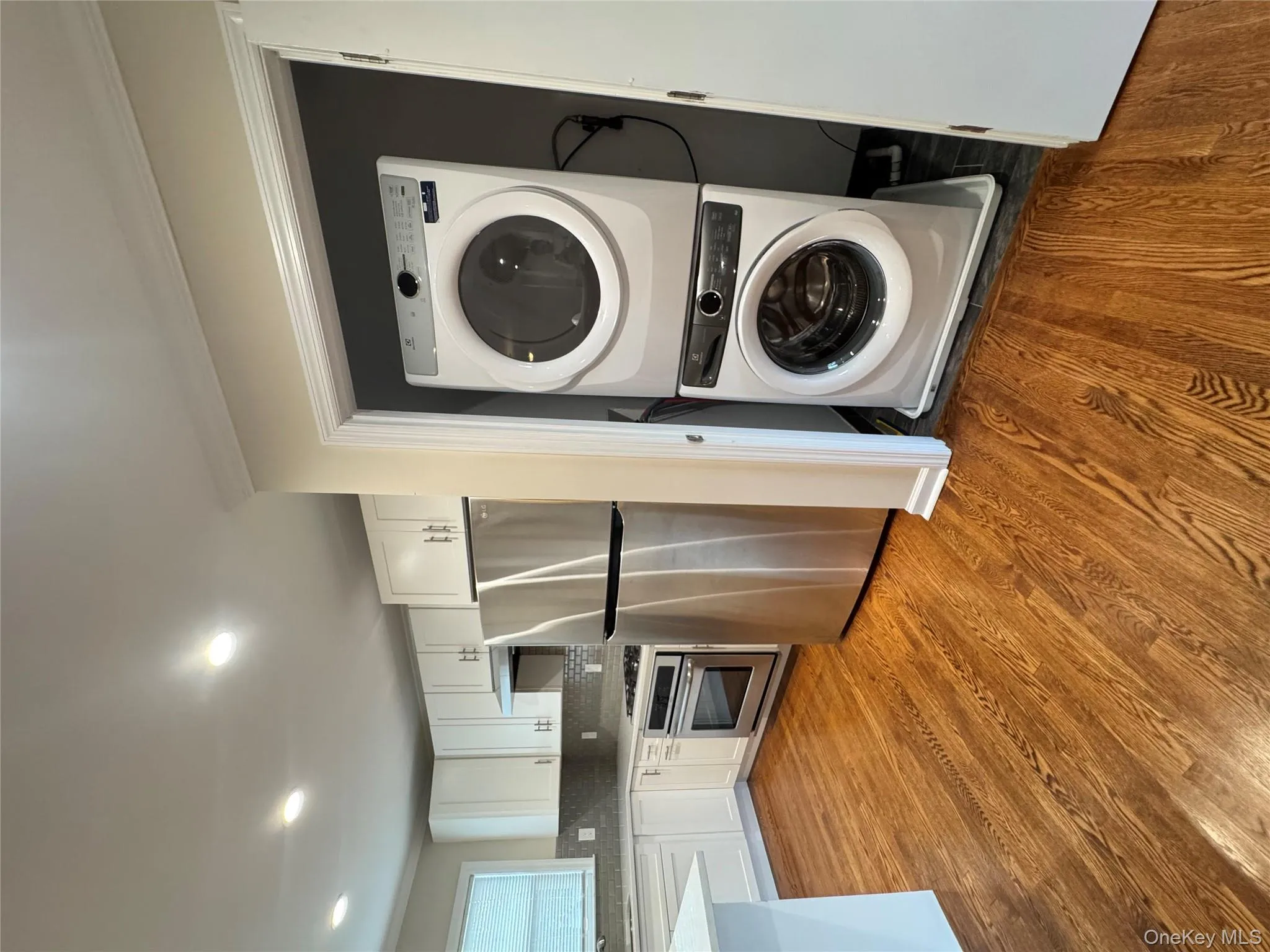 Laundry area featuring dark wood finished floors, stacked washer / drying machine, crown molding, and recessed lighting Laundry area featuring dark wood finished floors, stacked washer / drying machine, crown molding, and recessed lighting