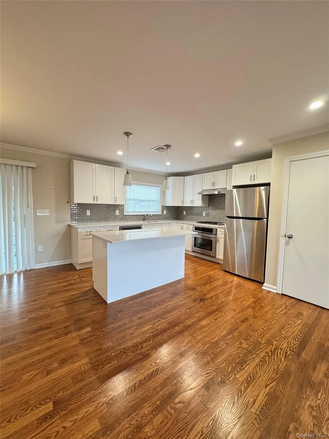 Kitchen featuring ornamental molding, white cabinetry, decorative light fixtures, appliances with stainless steel finishes, and a center island Kitchen featuring ornamental molding, white cabinetry, decorative light fixtures, appliances with stainless steel finishes, and a center island