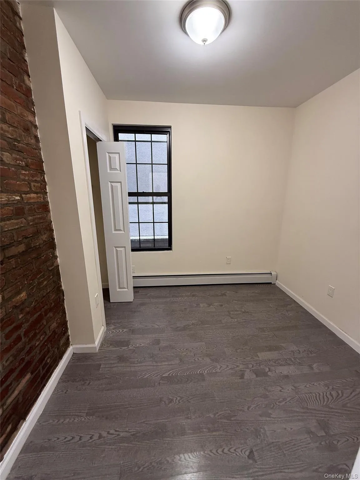Empty room with dark wood-style flooring, a baseboard heating unit, and brick wall Empty room with dark wood-style flooring, a baseboard heating unit, and brick wall