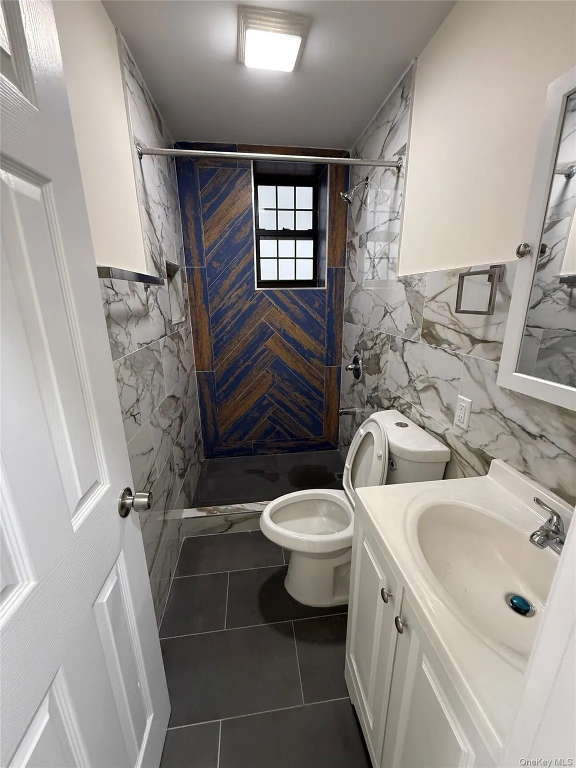 Bathroom with vanity, tile walls, a shower stall, and dark tile patterned floors Bathroom with vanity, tile walls, a shower stall, and dark tile patterned floors