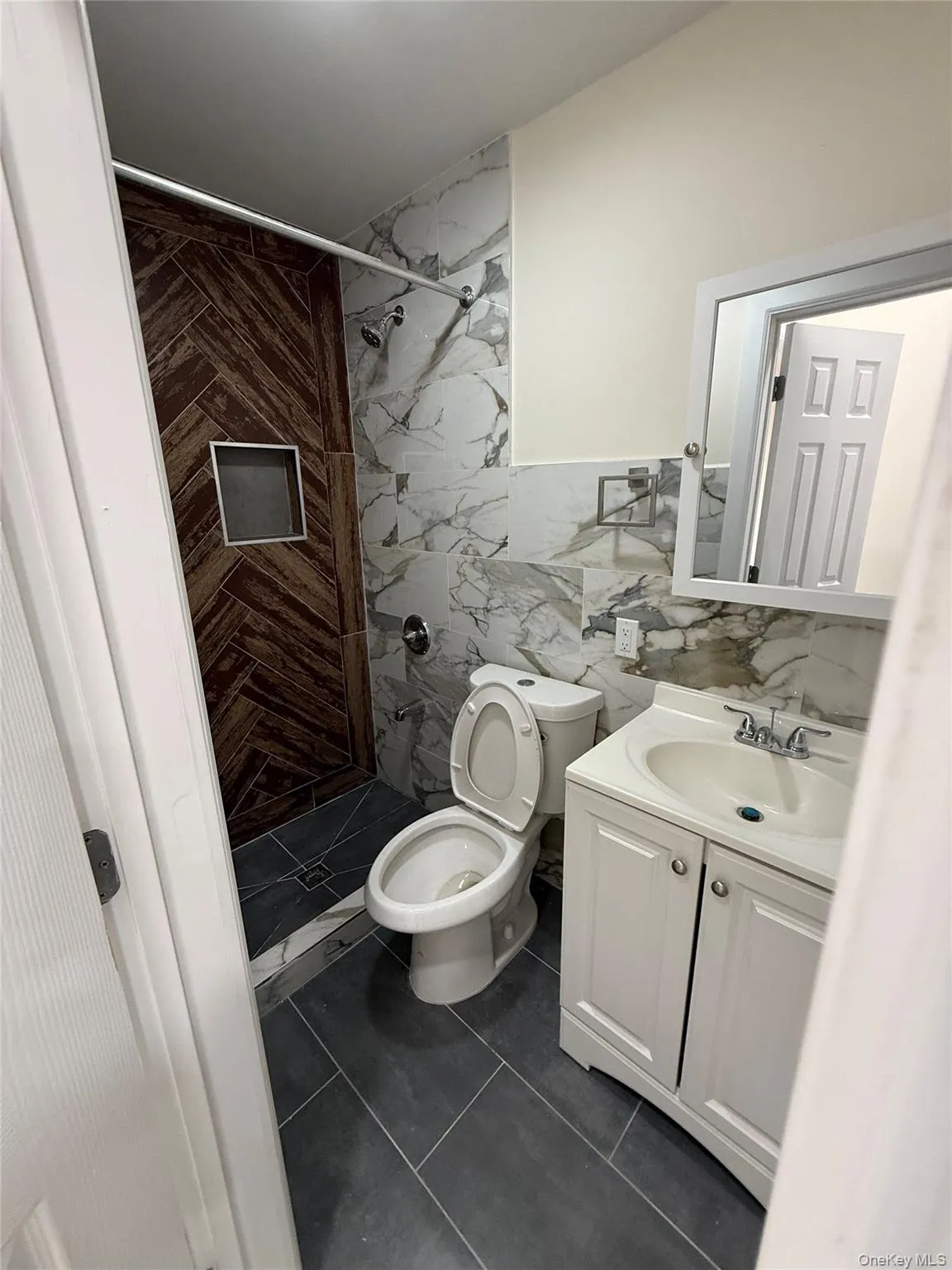 Bathroom featuring tile walls, vanity, a stall shower, and dark tile patterned flooring Bathroom featuring tile walls, vanity, a stall shower, and dark tile patterned flooring