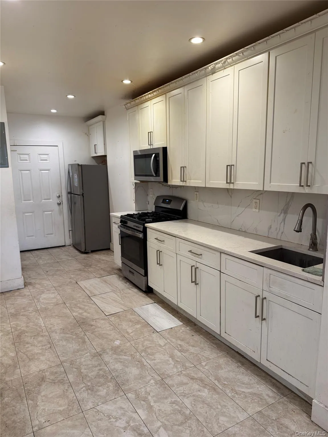 Kitchen featuring stainless steel appliances, white cabinets, recessed lighting, decorative backsplash, and light stone counters Kitchen featuring stainless steel appliances, white cabinets, recessed lighting, decorative backsplash, and light stone counters