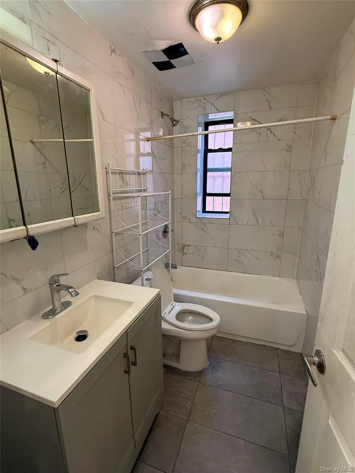 Full bath featuring tile walls, shower / bathtub combination, vanity, and dark tile patterned flooring Full bath featuring tile walls, shower / bathtub combination, vanity, and dark tile patterned flooring