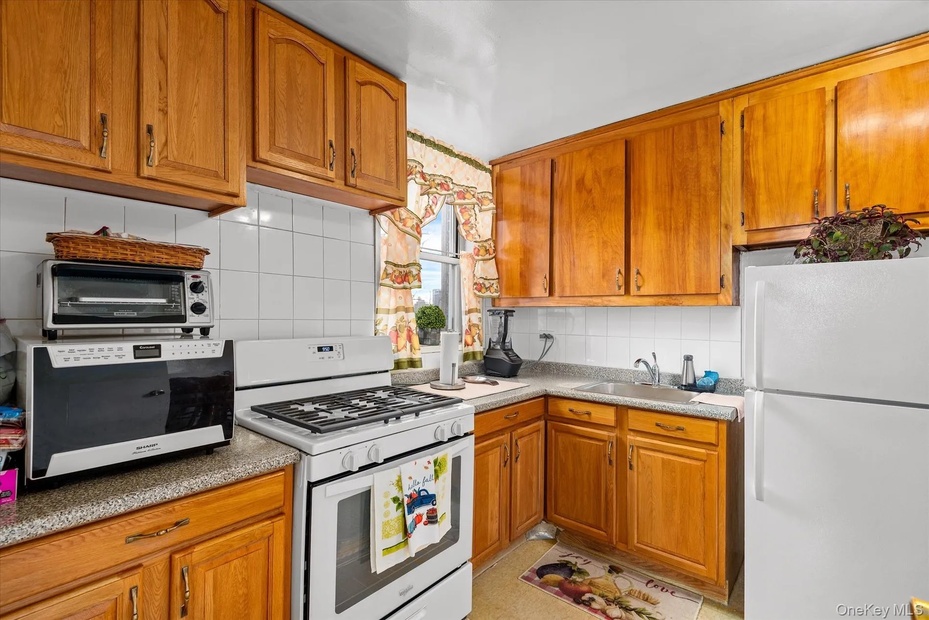Kitchen featuring white appliances, brown cabinetry, and decorative backsplash Kitchen featuring white appliances, brown cabinetry, and decorative backsplash
