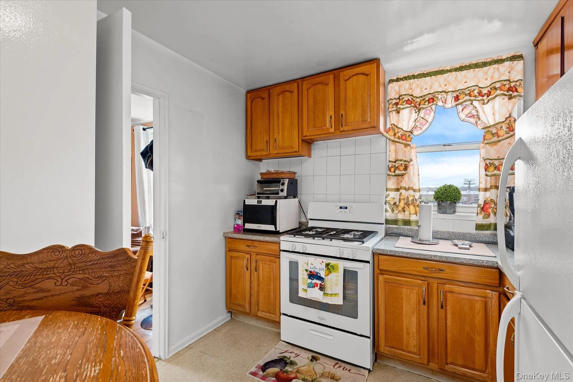 Kitchen featuring white appliances, brown cabinetry, tasteful backsplash, and light countertops Kitchen featuring white appliances, brown cabinetry, tasteful backsplash, and light countertops