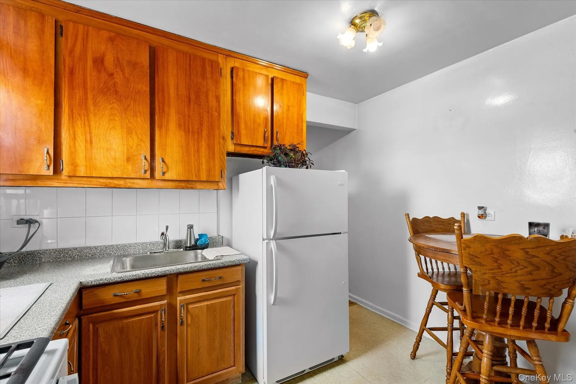 Kitchen featuring decorative backsplash, white appliances, brown cabinetry, light countertops, and light flooring Kitchen featuring decorative backsplash, white appliances, brown cabinetry, light countertops, and light flooring