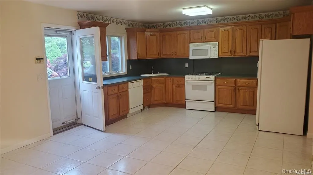 Kitchen with white appliances, dark countertops, brown cabinets, and light tile patterned flooring Kitchen with white appliances, dark countertops, brown cabinets, and light tile patterned flooring