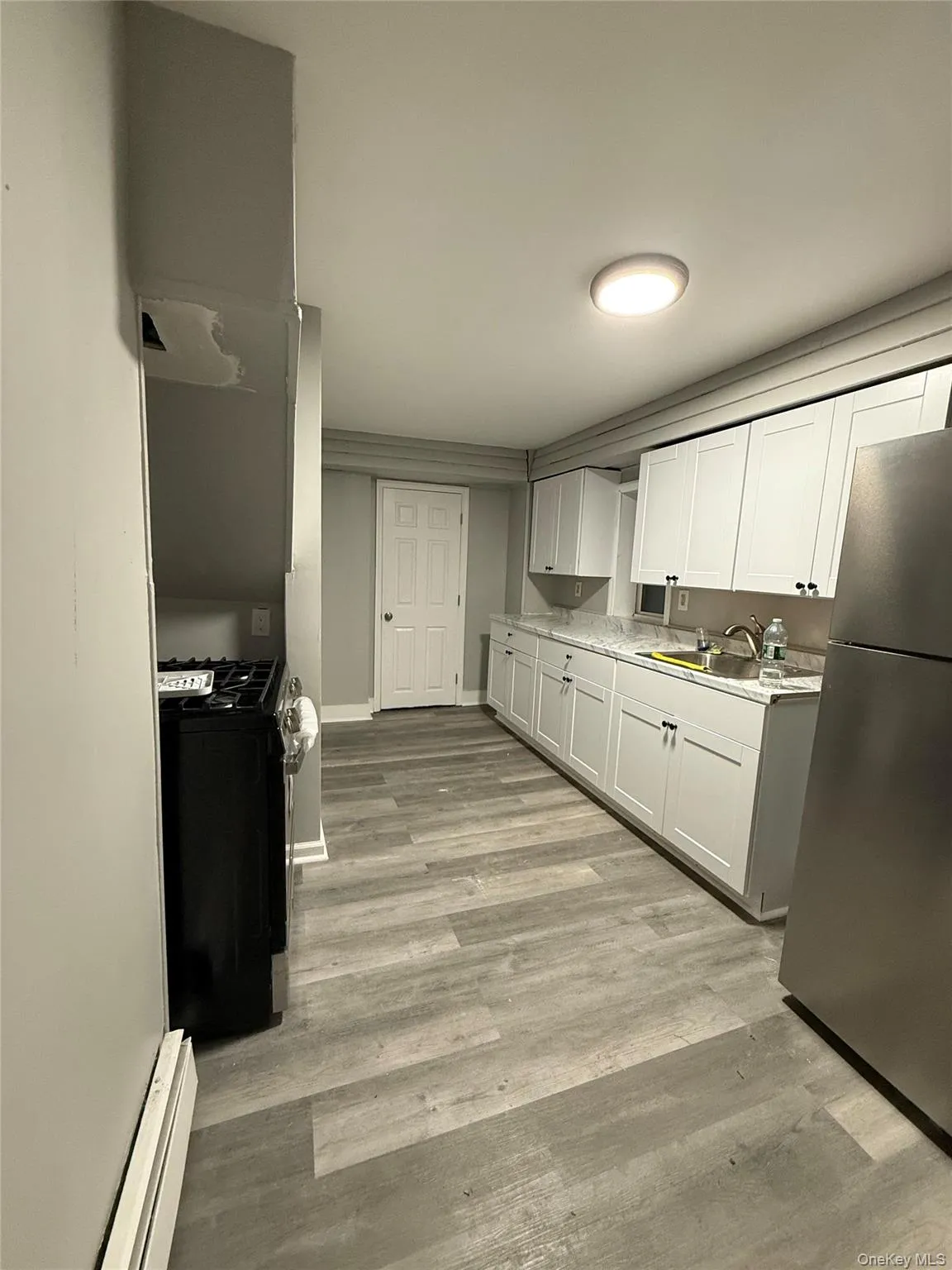 Kitchen featuring light countertops, stainless steel appliances, light wood-style floors, a baseboard heating unit, and white cabinetry Kitchen featuring light countertops, stainless steel appliances, light wood-style floors, a baseboard heating unit, and white cabinetry