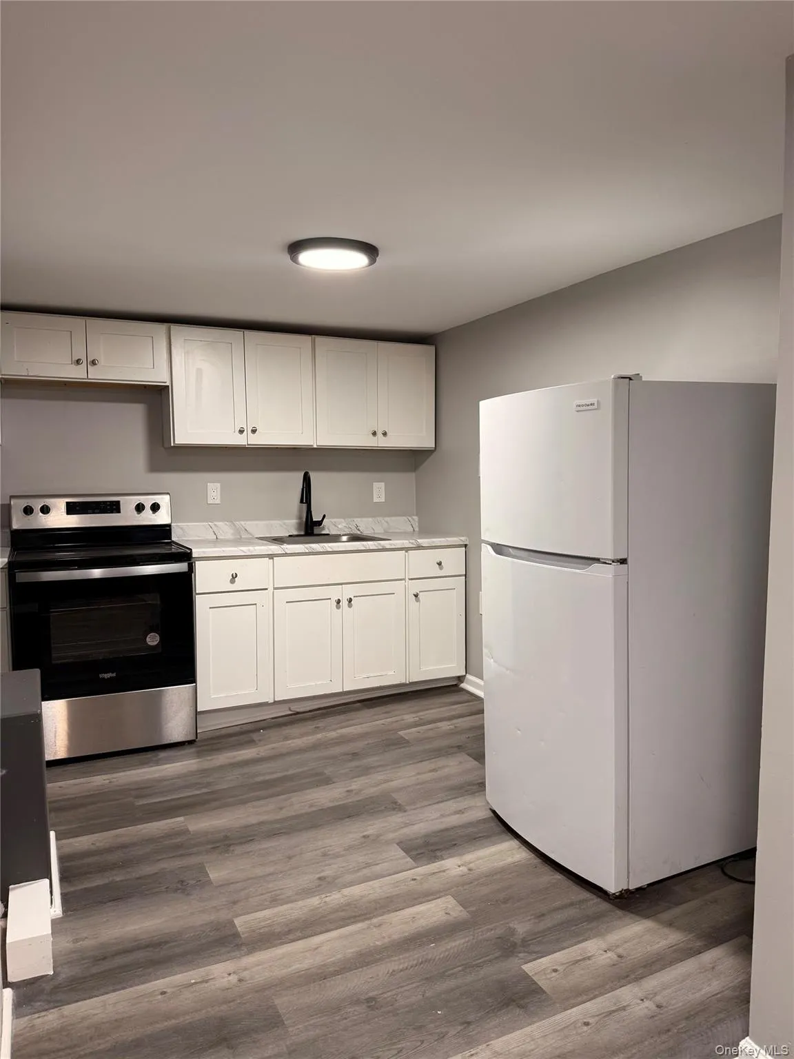 Kitchen with freestanding refrigerator, stainless steel electric stove, white cabinets, light countertops, and dark wood-style flooring Kitchen with freestanding refrigerator, stainless steel electric stove, white cabinets, light countertops, and dark wood-style flooring
