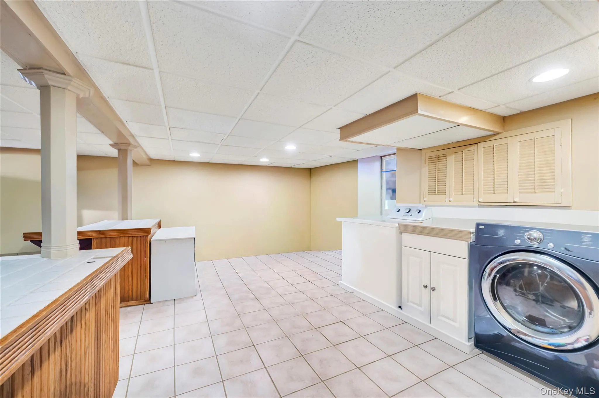 Laundry area with washer / clothes dryer, recessed lighting, light tile patterned floors, a paneled ceiling, and cabinet space Laundry area with washer / clothes dryer, recessed lighting, light tile patterned floors, a paneled ceiling, and cabinet space